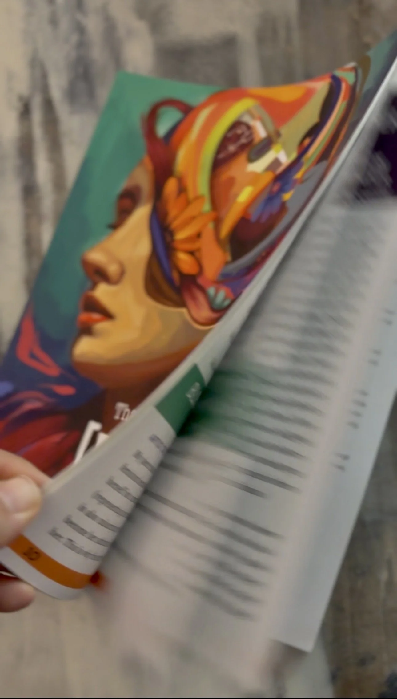 A person flipping through a magazine featuring an artistic illustration of a woman's face with colorful abstract elements.