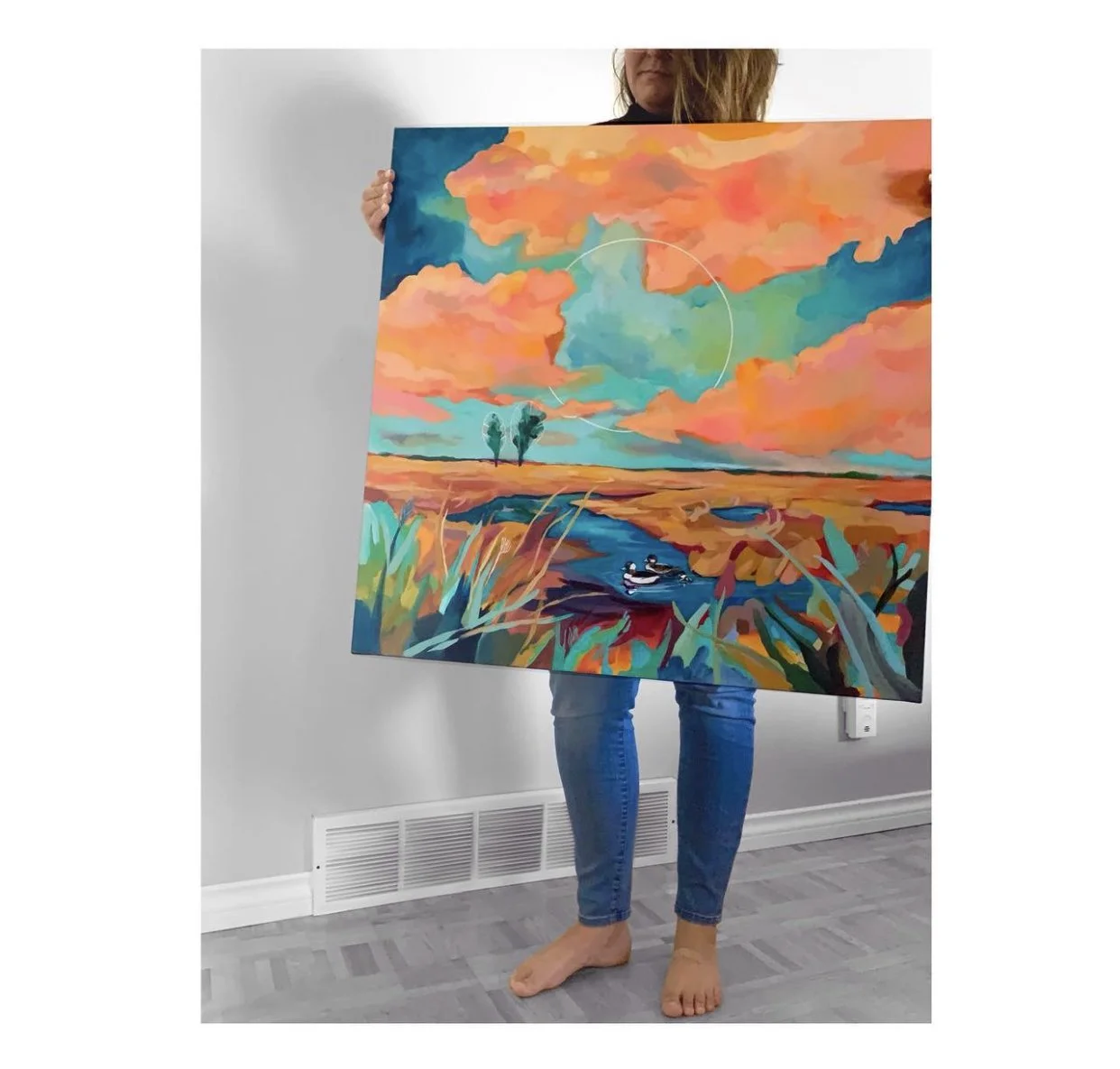 Person holding a colorful landscape painting with sky, clouds, trees, a river, and three ducks. Kelowna BC. Liz Grace Studio, Liz Dumontet