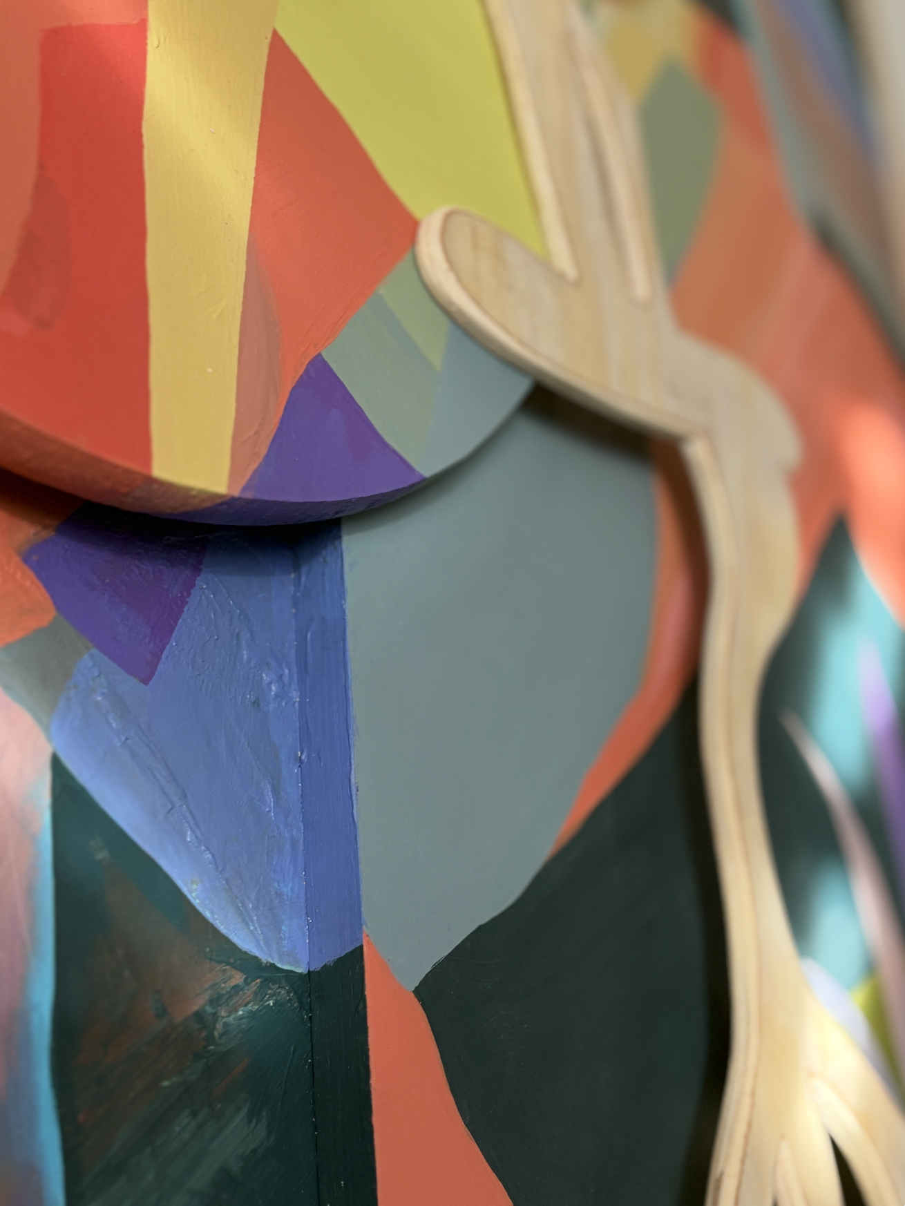 Close-up of a colorful, abstract painted surface with curved edges and a three-dimensional wooden element.