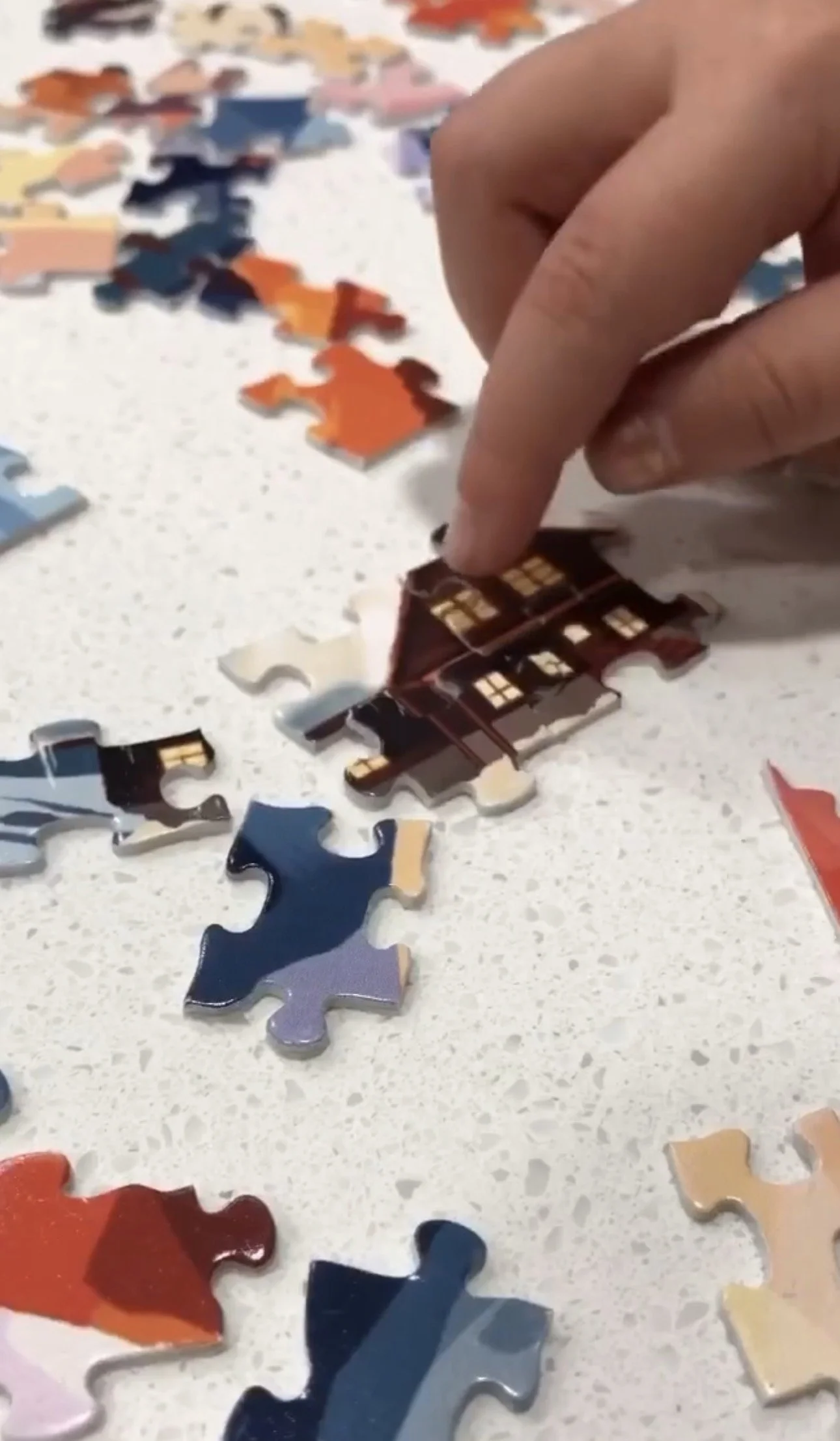 Close-up of a hand assembling a jigsaw puzzle with colorful pieces on a white surface.
