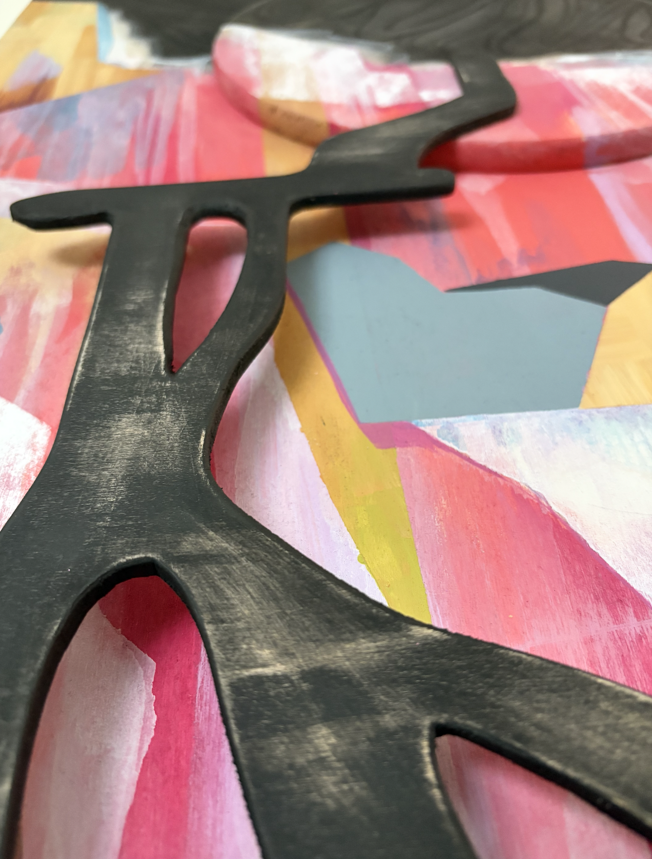 Close-up of a black, wooden waterfall, wooden painting placed on an abstract, colorful painted surface.  Kelowna BC. Liz Grace Studio, Liz Dumontet