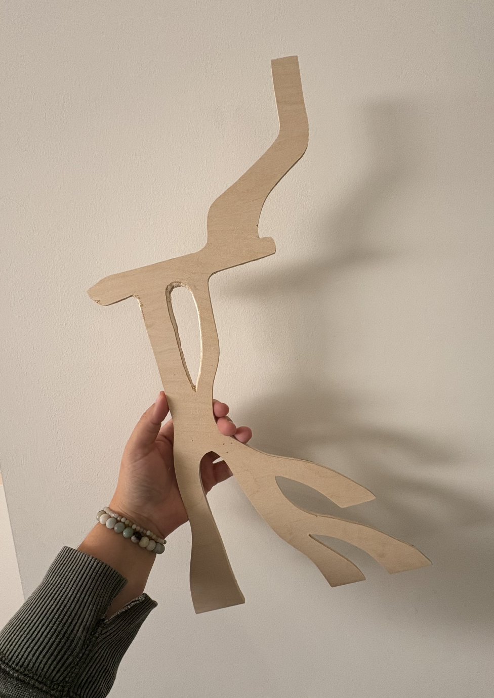 A person holding a wooden cutout shaped like a waterfall against a plain wall.