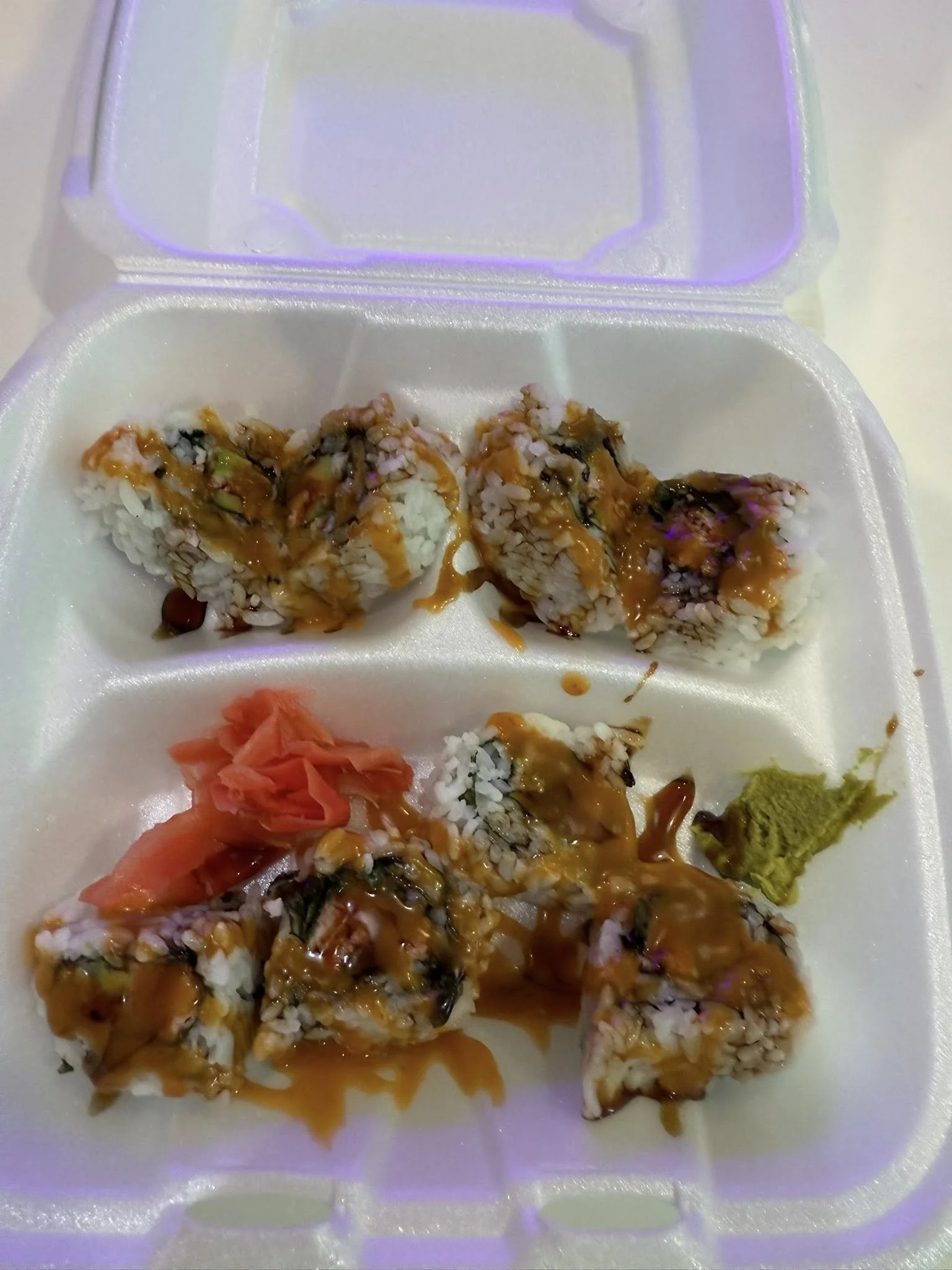 Six pieces of sushi rolls with sauce, pickled ginger, and wasabi in a foam takeout container.