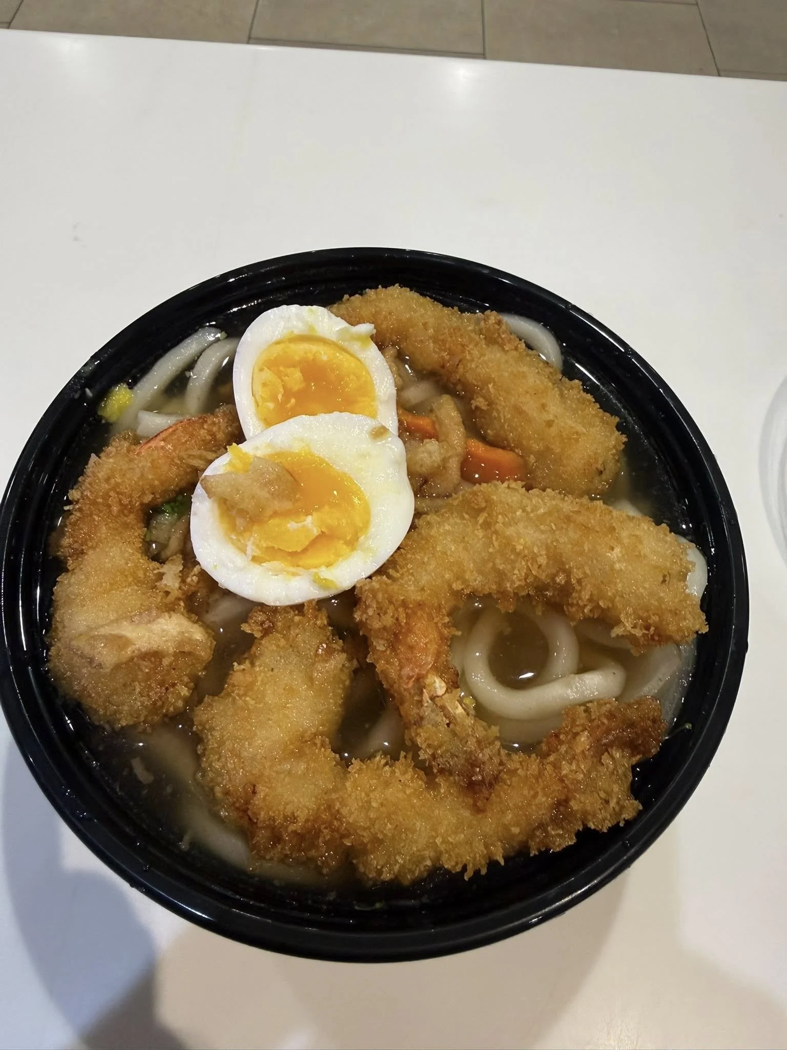 Bowl of noodle soup with fried fish fillets, halved boiled eggs, and vegetables.