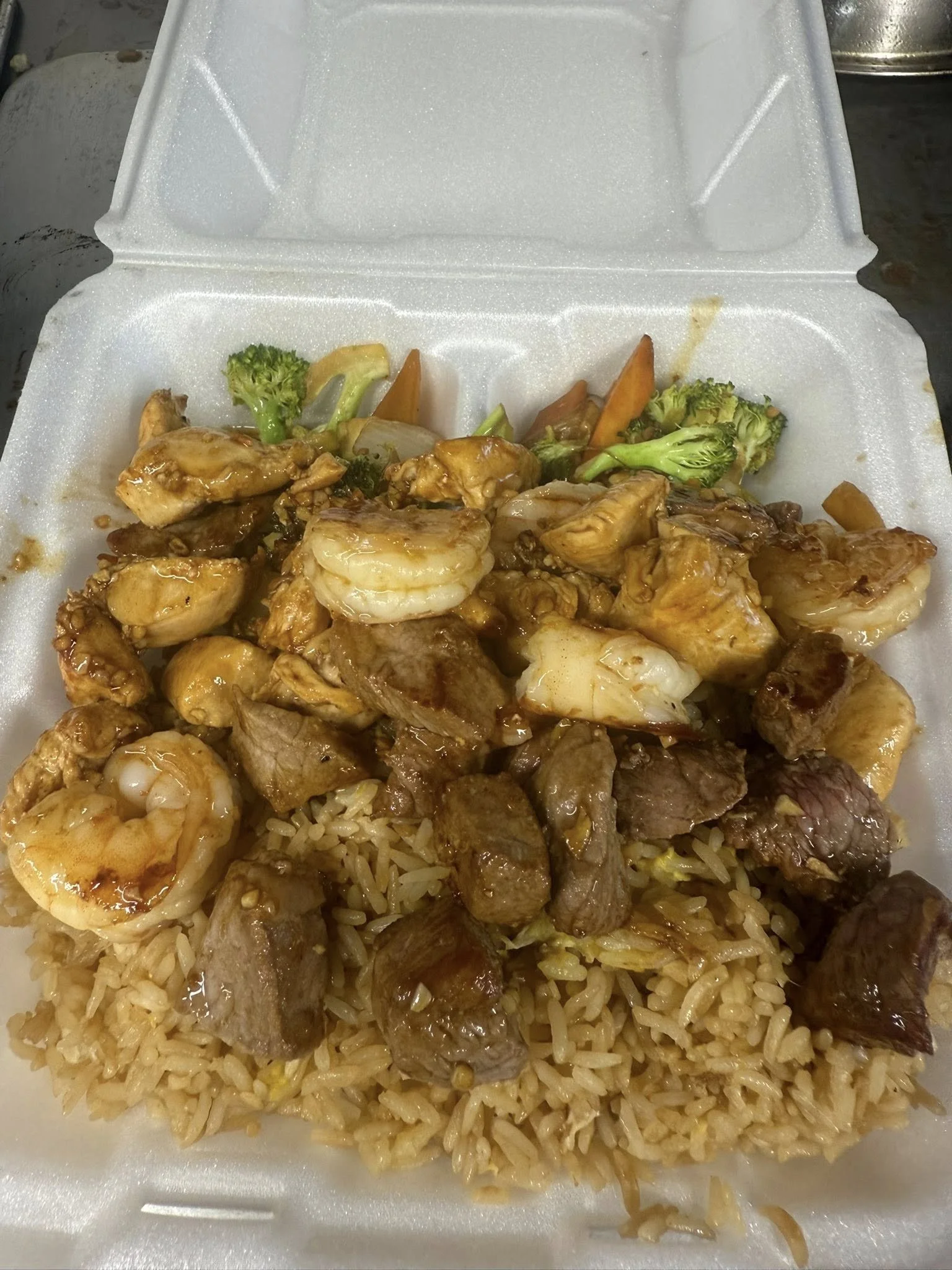 Chinese takeout box with fried rice topped with shrimp, beef, chicken, and vegetables.