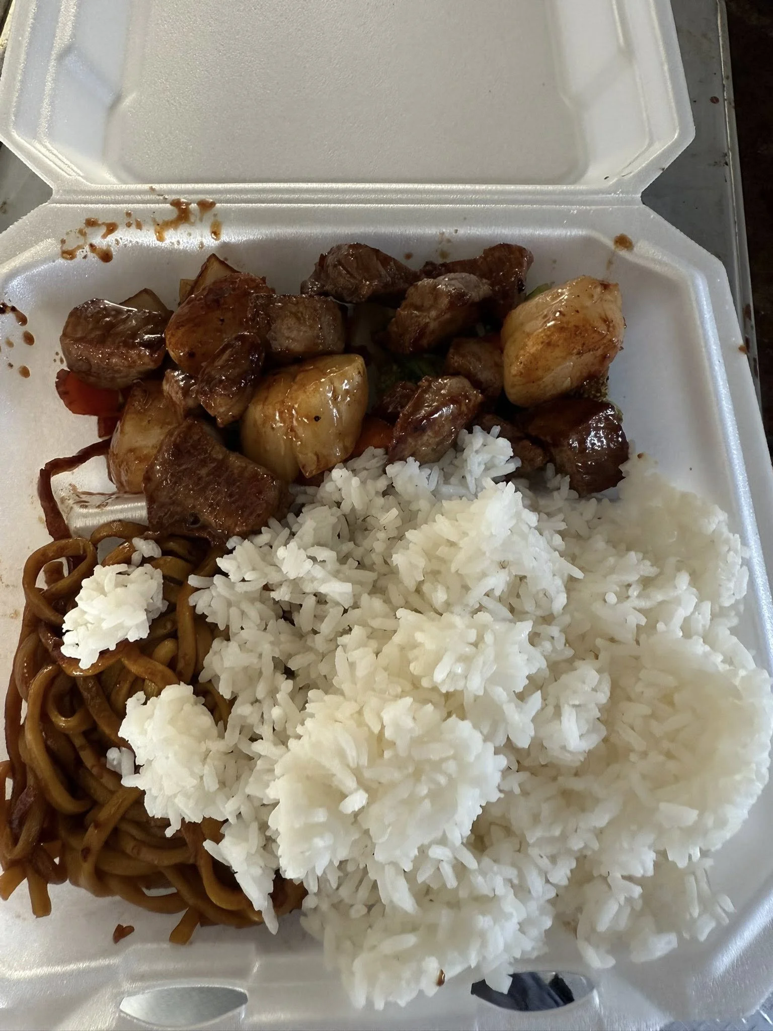 Takeout container with white rice, stir-fried noodles, and stir-fried meat with vegetables
