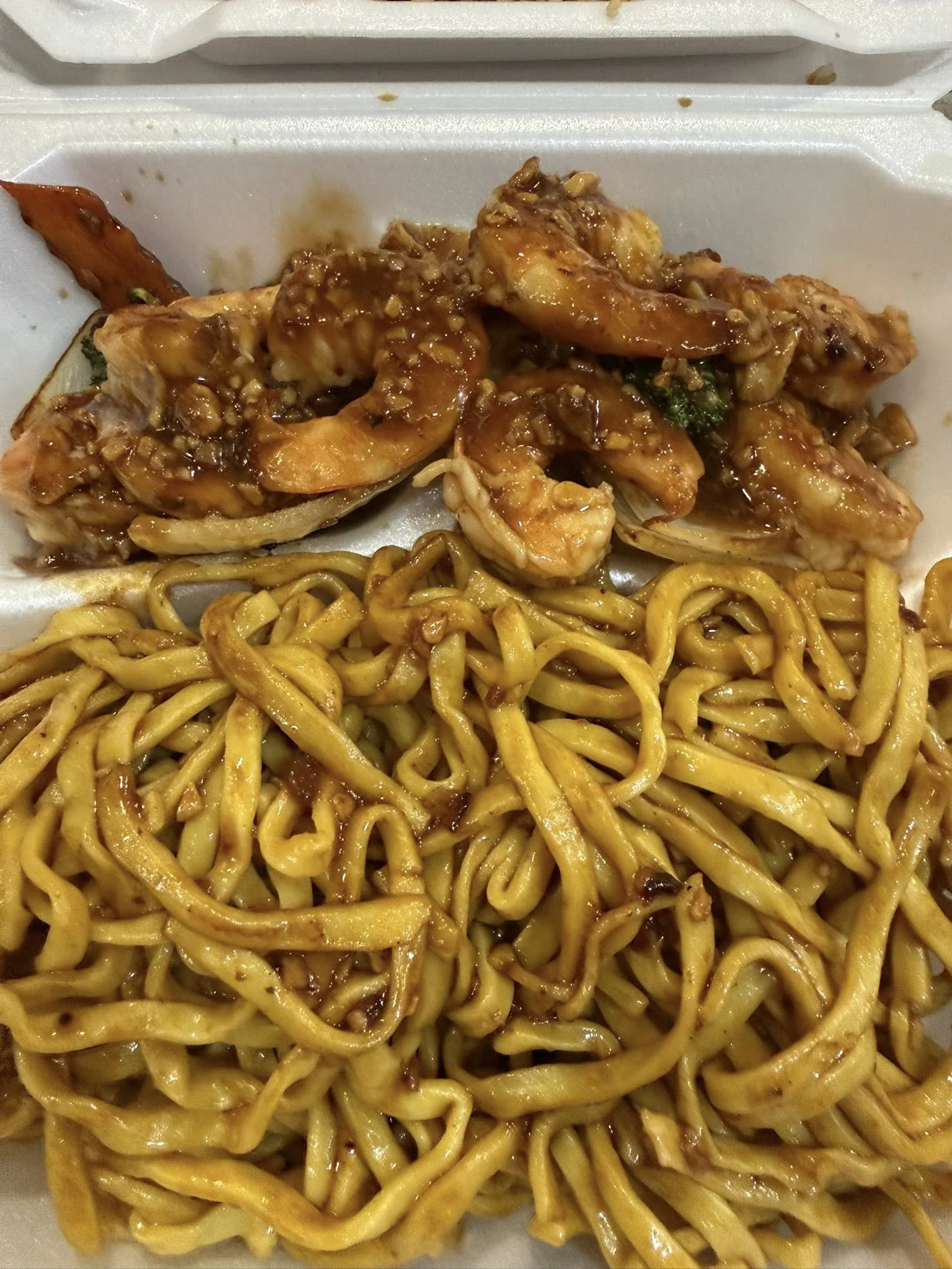 Takeout box containing cooked shrimp with sauce and a portion of stir-fried noodles.
