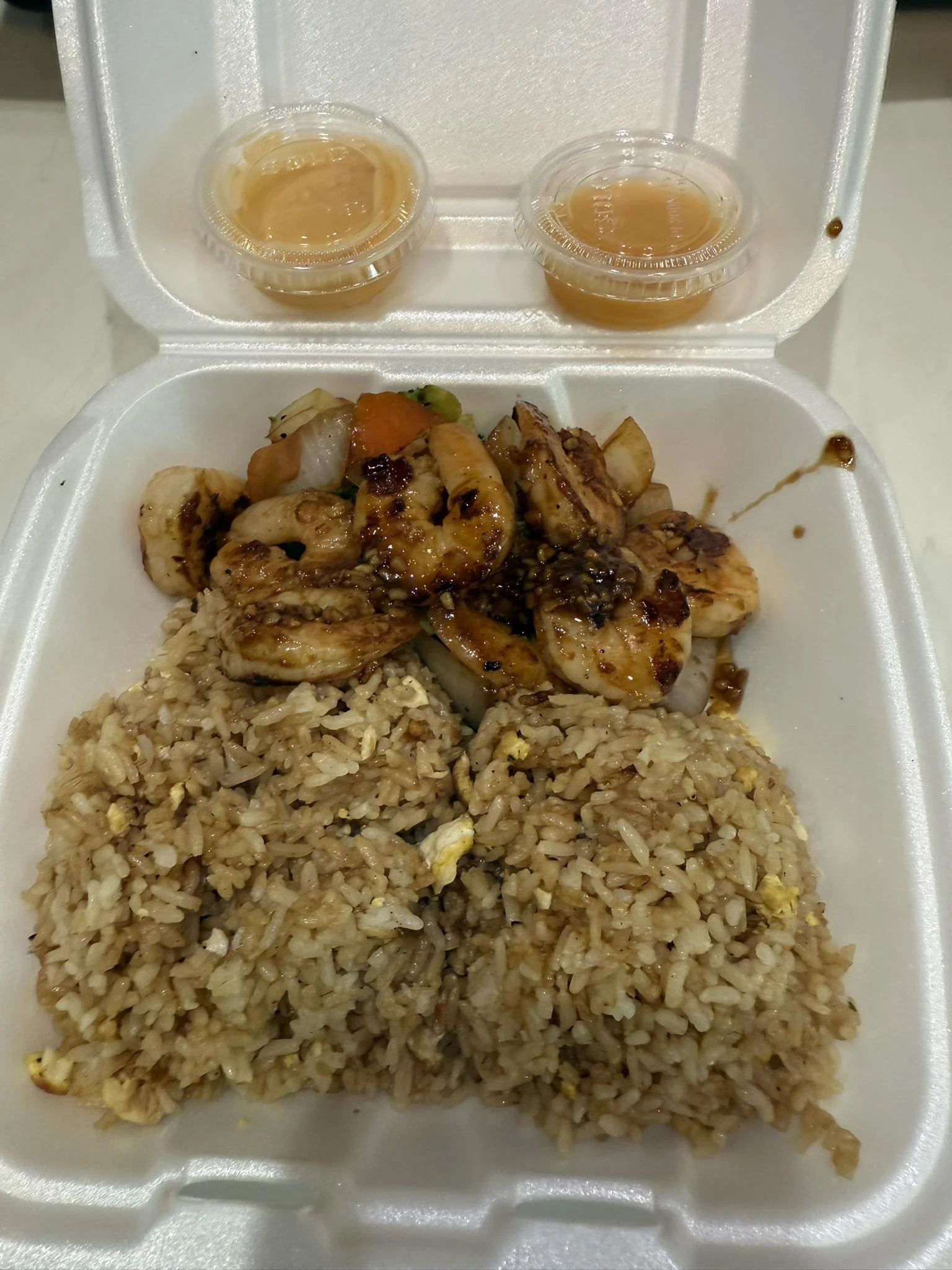 Foam container with fried rice, grilled chicken, shrimp, vegetables, and two small cups of sauce.