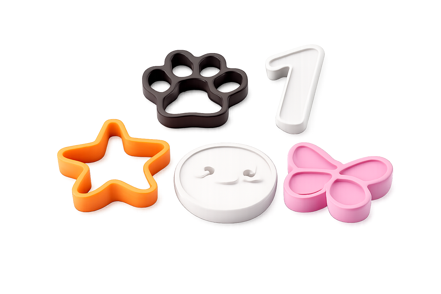 Colorful cookie cutters in various shapes and colors, including a black paw print, orange star, white number one, pink butterfly, and white smiling face, arranged on a reflective surface.
