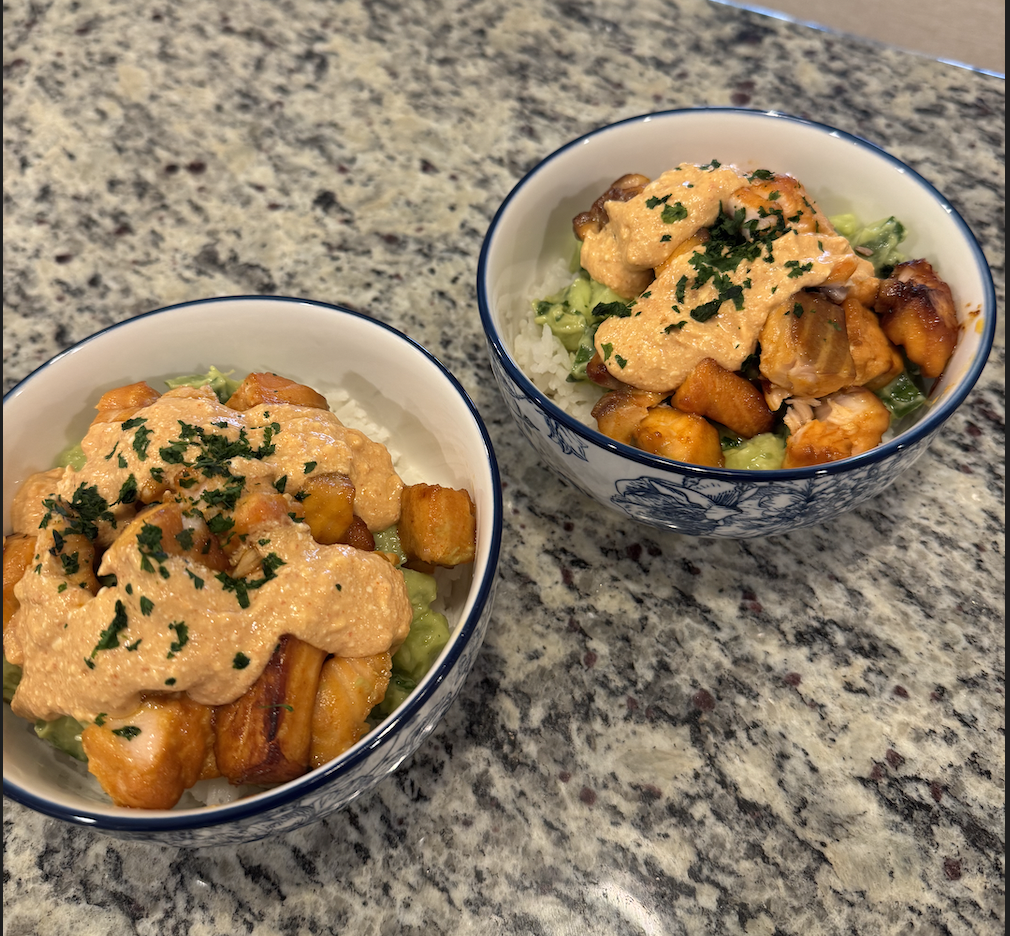 Two bowls of food containing roasted sweet potatoes, lettuce, and a creamy sauce topped with chopped parsley, on a granite countertop.