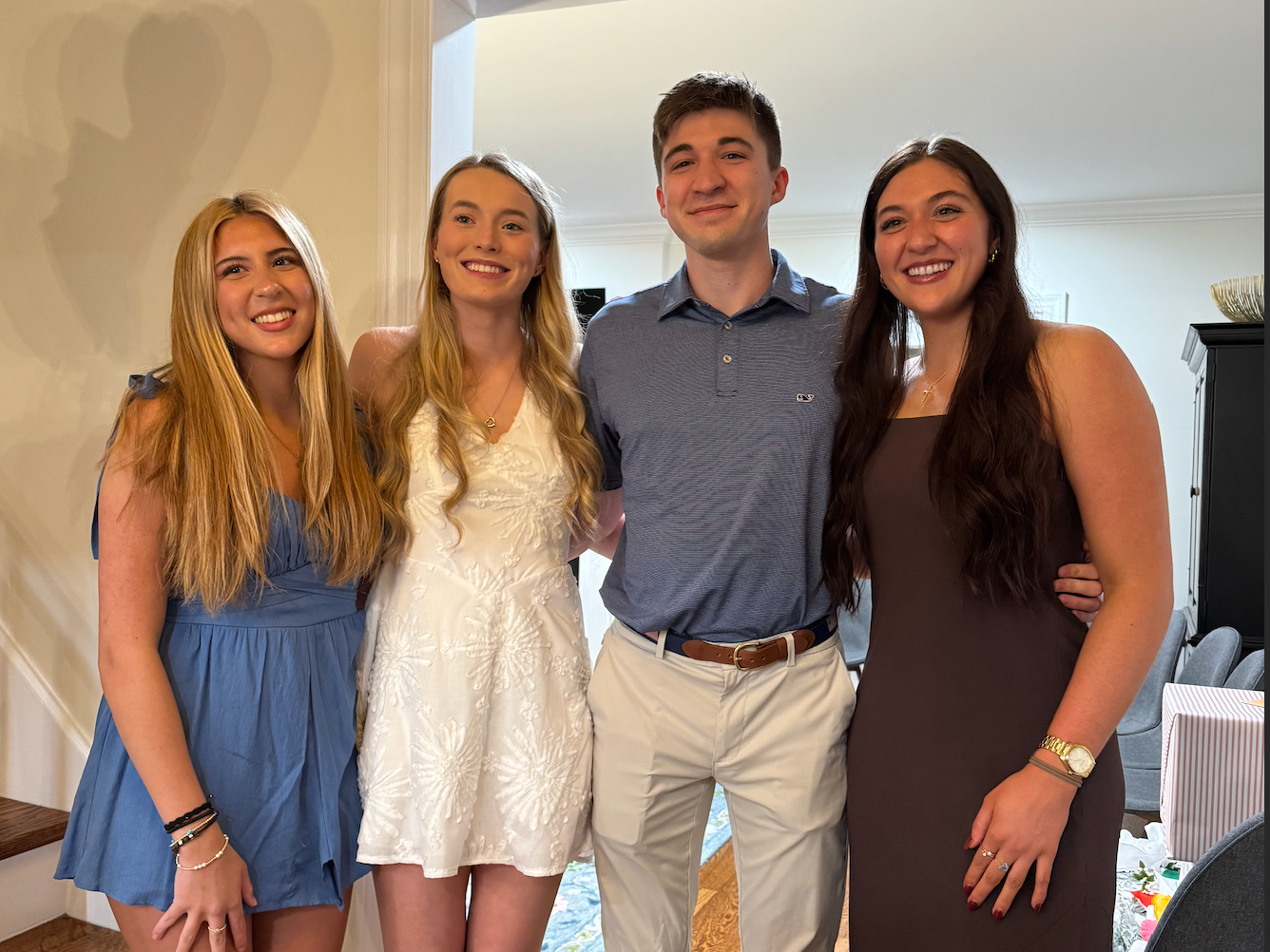 Four young adults smiling and standing close together indoors, with two women on each side of a man.