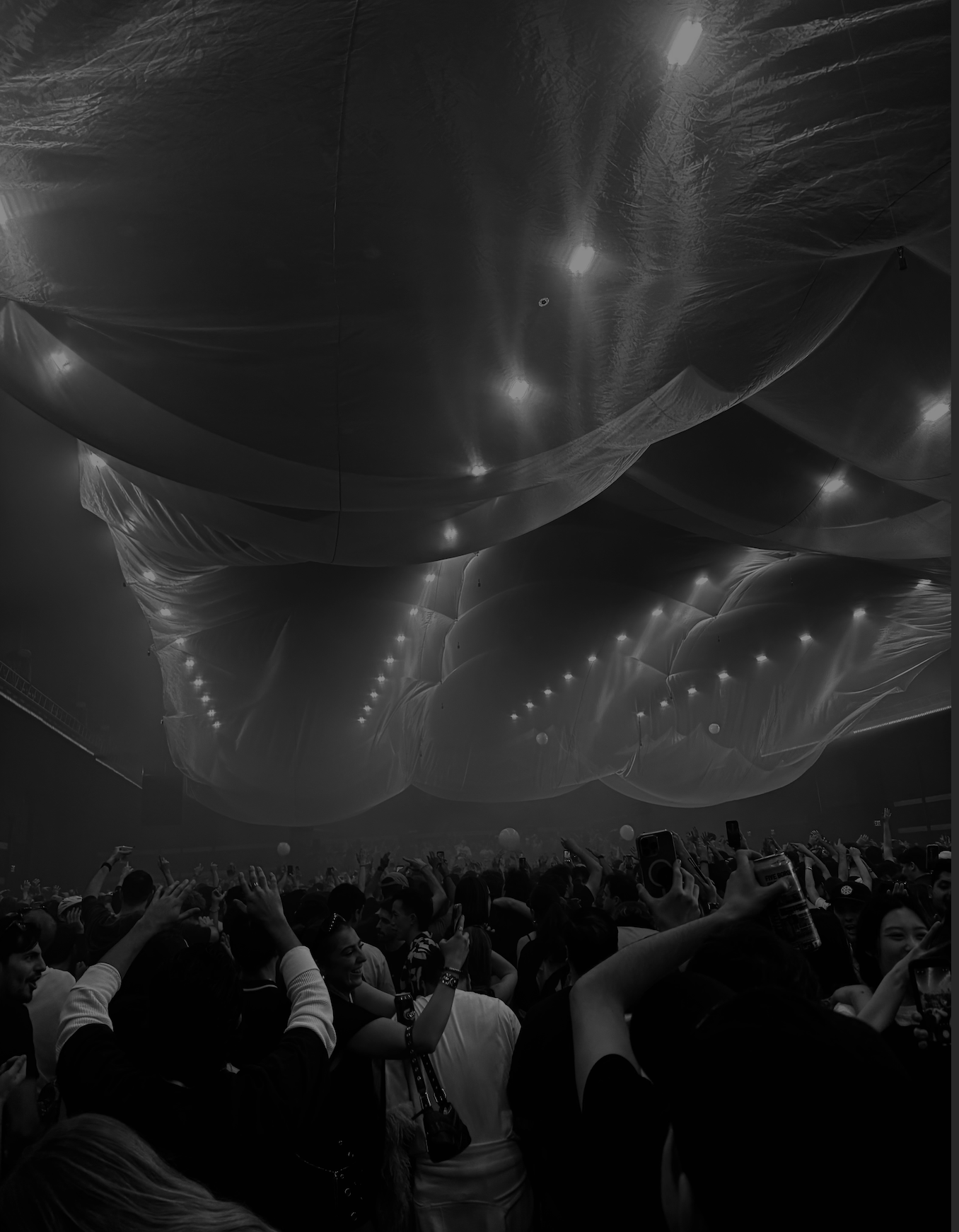 Crowd of people at a concert or event with inflated balloons or structures hanging from the ceiling.