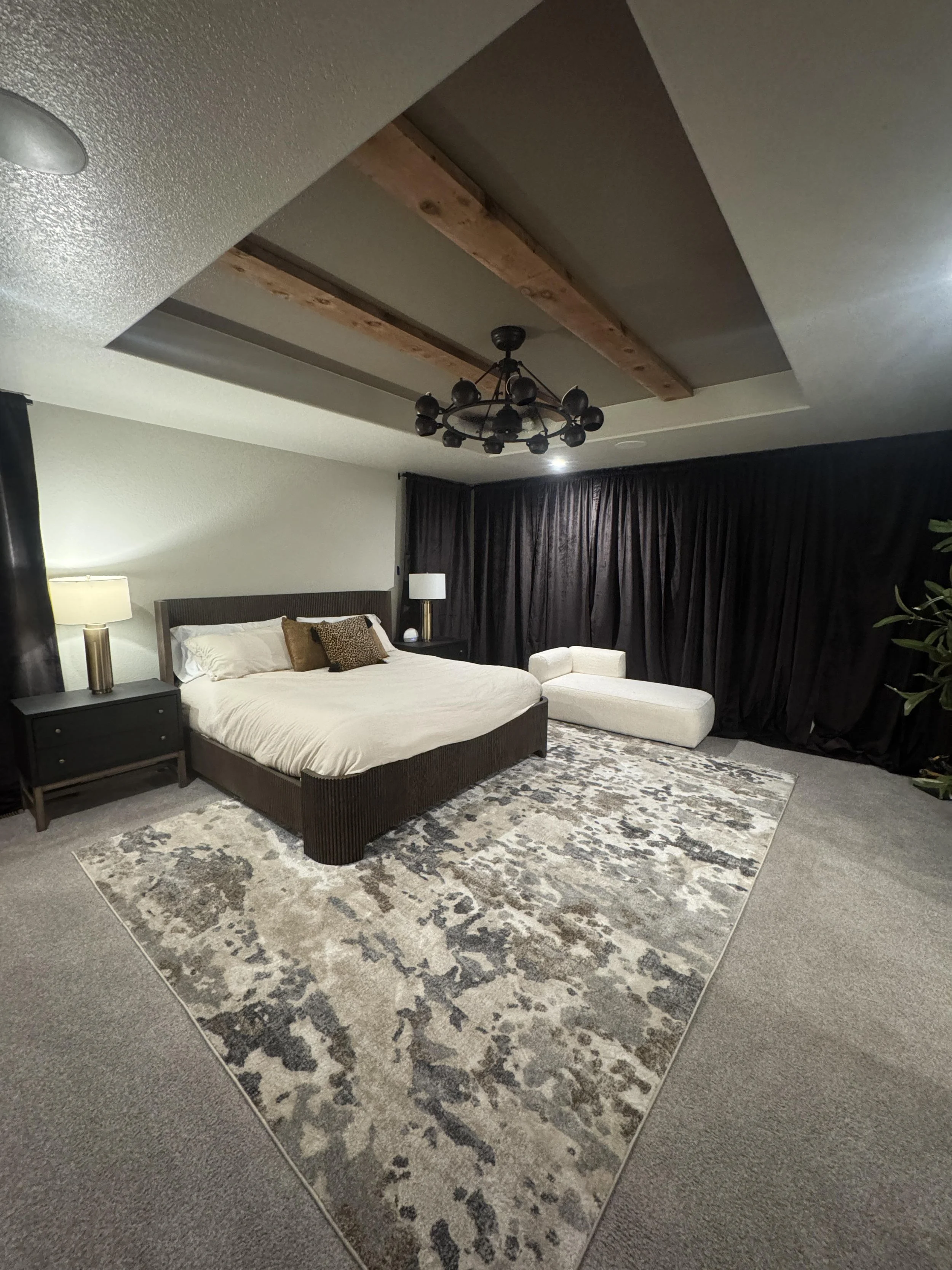 A modern bedroom with a king-sized bed. A chandelier hangs from a recessed ceiling with wooden beams. European Design. Interior Design. Dallas. Highland Park. North Dallas. Great room. renovation. Remodel. custom craftsmanship. Timeless.