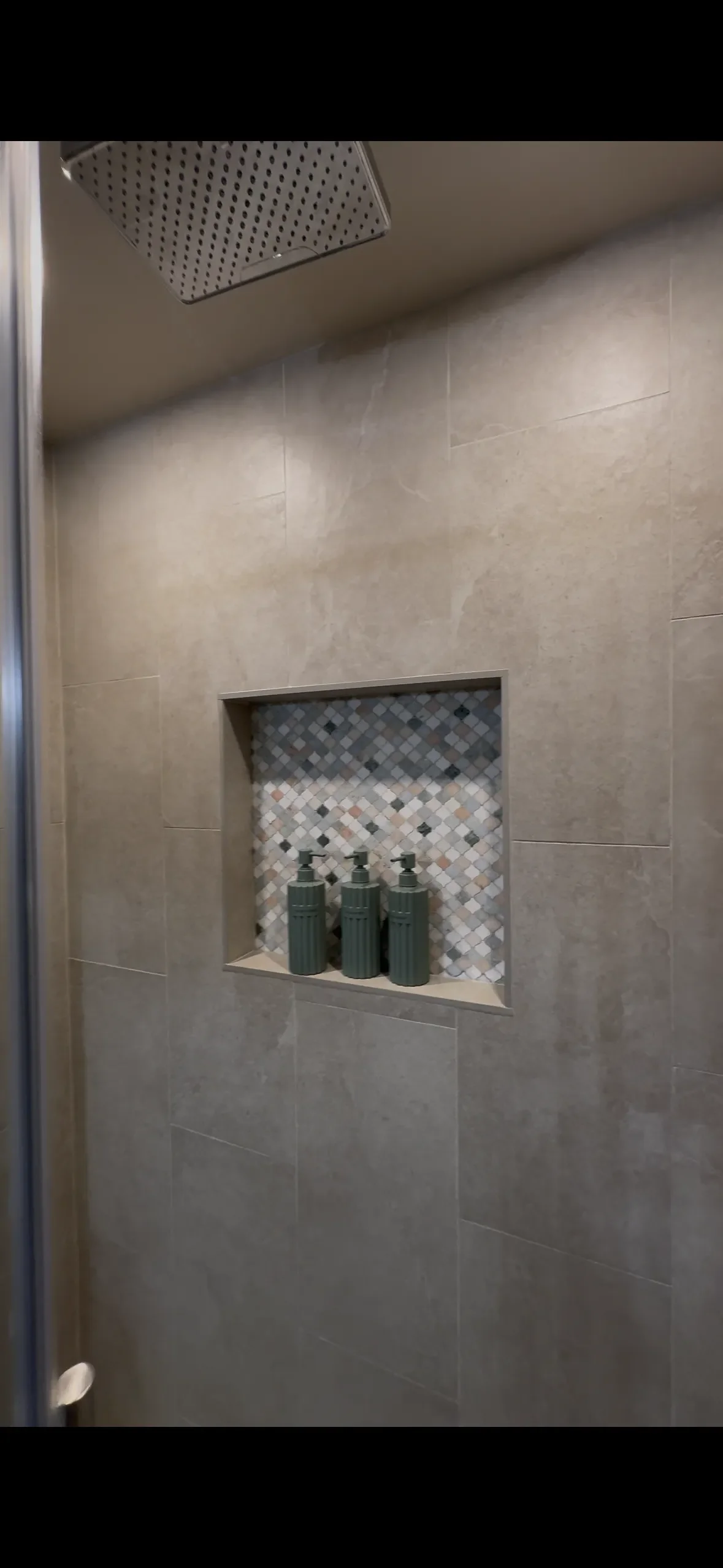 A shower wall with beige tiles, a built-in niche with small mosaic tiles, and three green soap dispensers in the niche.European Design. Interior Design. Dallas. Highland Park. North Dallas. renovation. Remodel. custom craftsmanship. Timeless