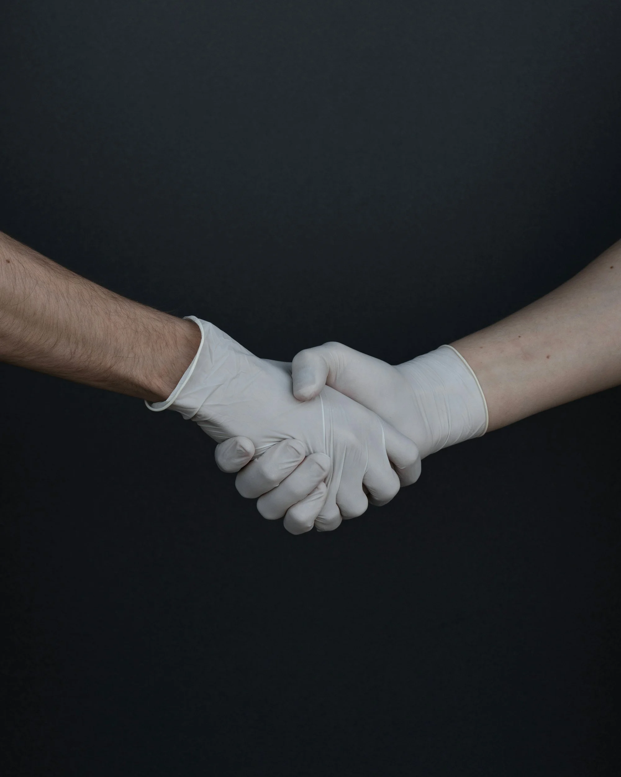 Two people wearing white gloves shaking hands against a black background.