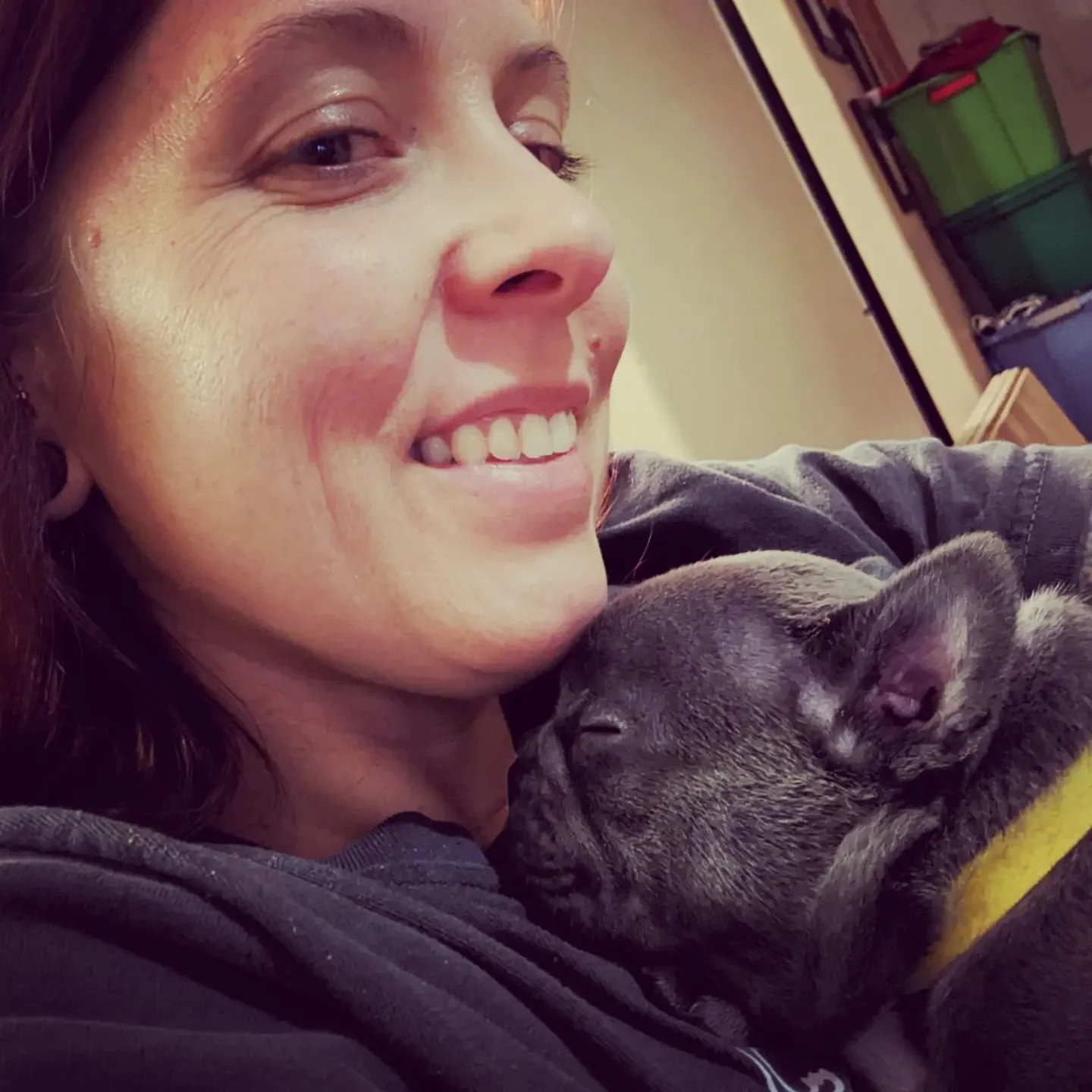 Close-up of a woman smiling with a brindle puppy sleeping on her chest.