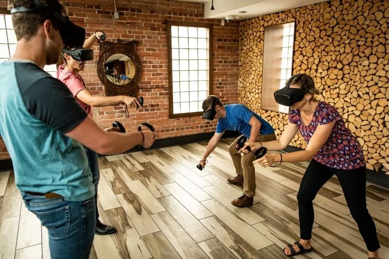 Four people in a room wearing virtual reality headsets and holding controllers, engaged in a virtual reality game or experience.