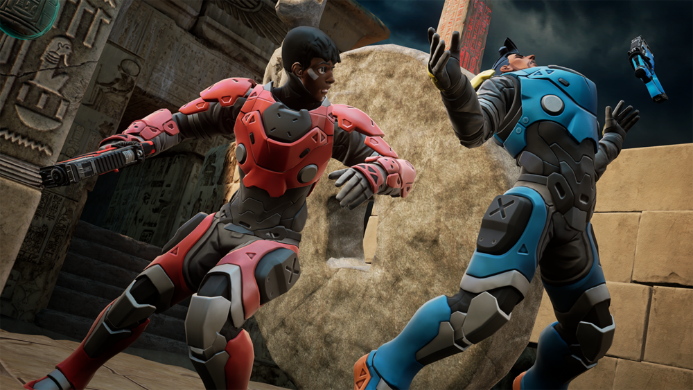 Two characters in futuristic armor engaged in a fight, one in red and black with a gun, the other in blue and black with arms raised, in an ancient Egyptian setting with hieroglyphs and stone structures. Virtual Reality Games