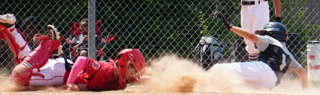A girl sliding into home plate while the catcher tries to tag her out during a softball game.