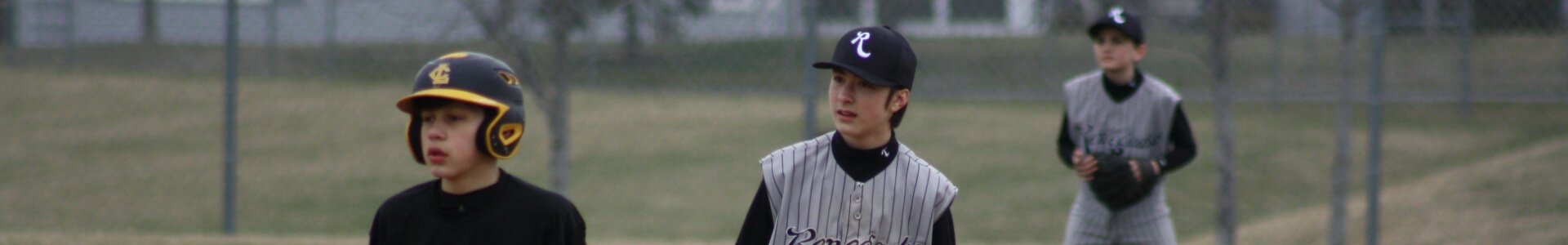 Three young boys playing baseball on a field, wearing baseball uniforms and caps.