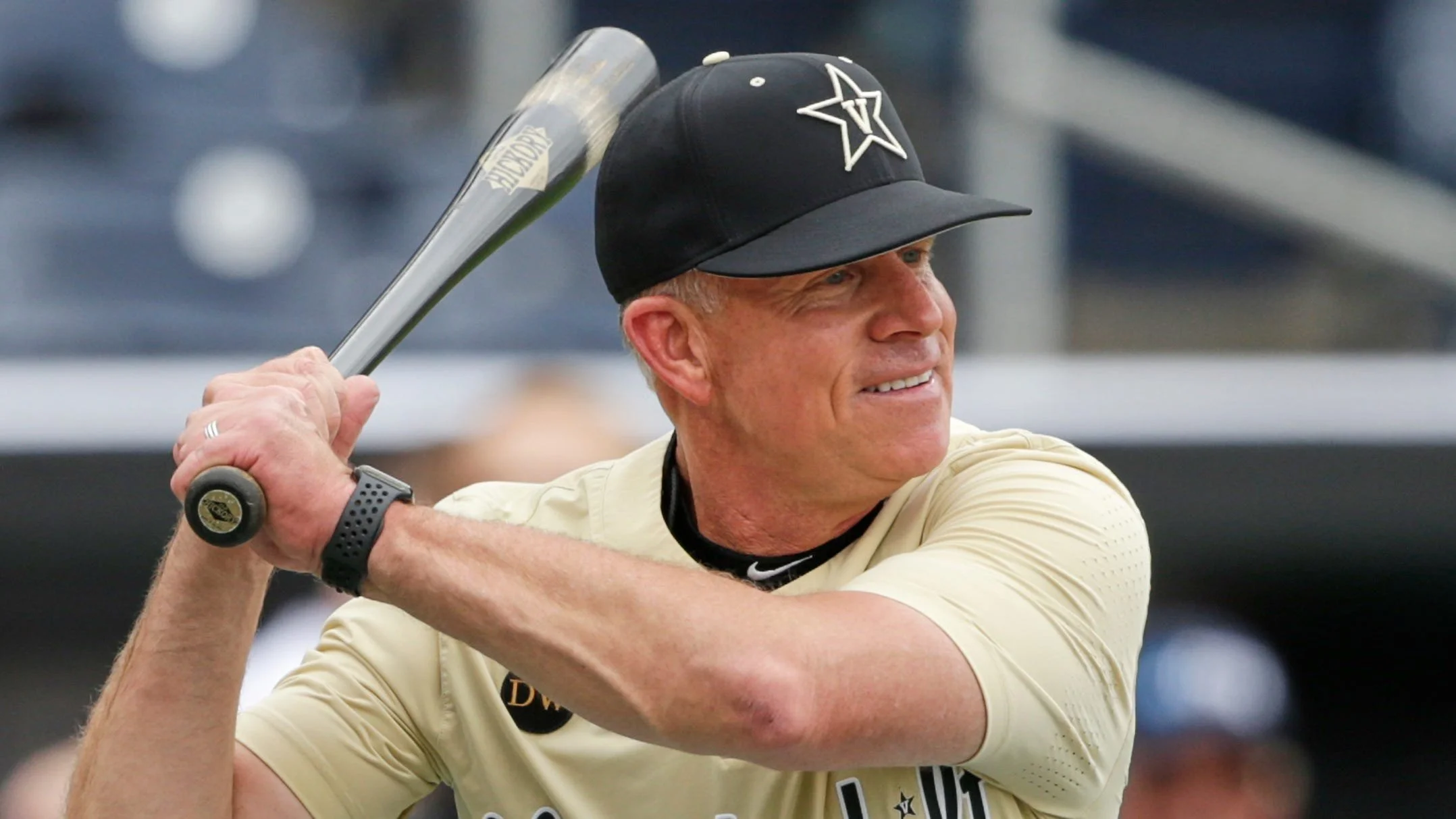 A man with a fair complexion and short blonde hair, wearing a black cap with a star logo, is holding a golf club. He is dressed in a light-colored shirt and is smiling as he prepares to swing.