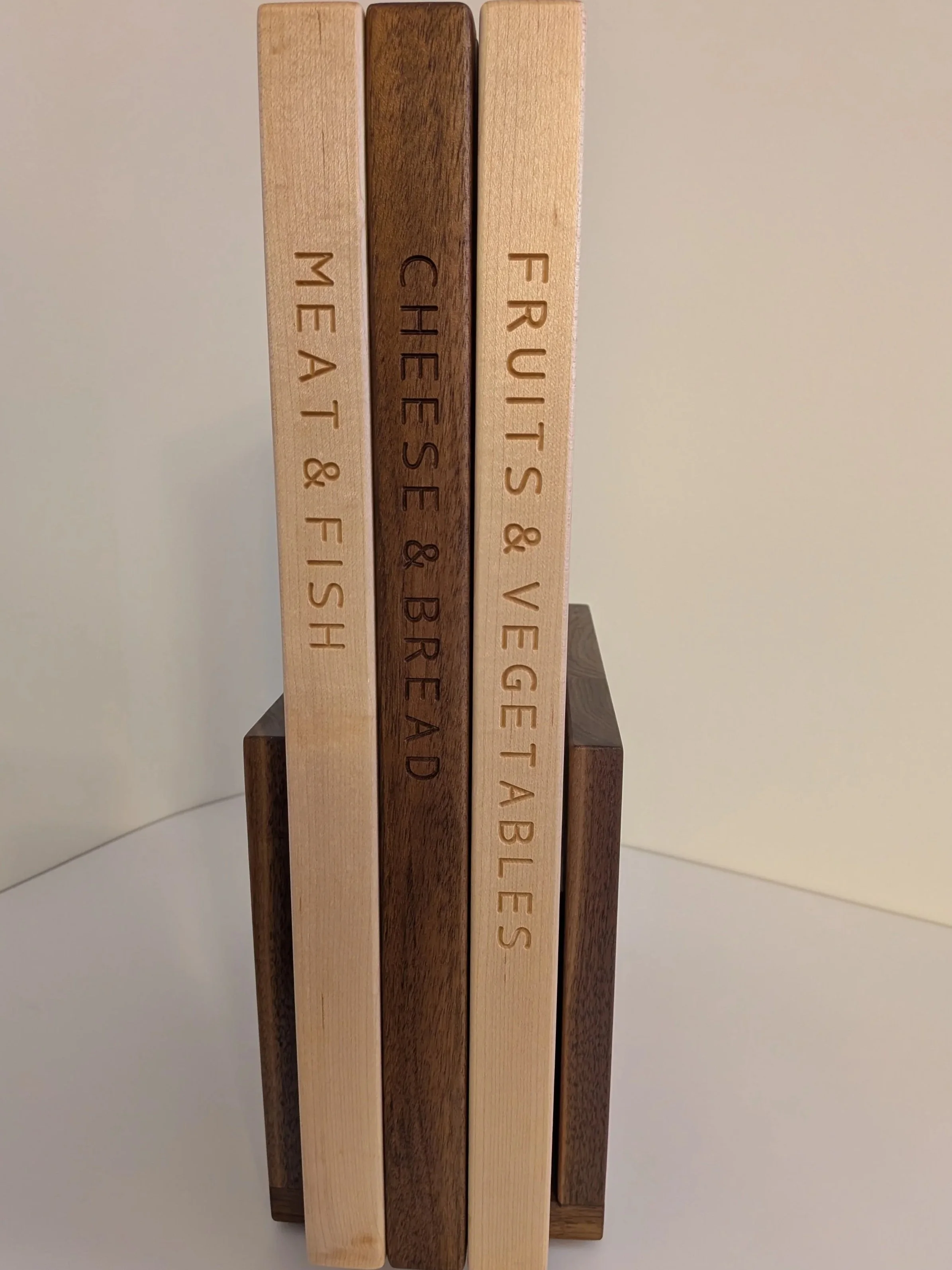 Walnut and maple cutting boards displayed like books in a walnut stand