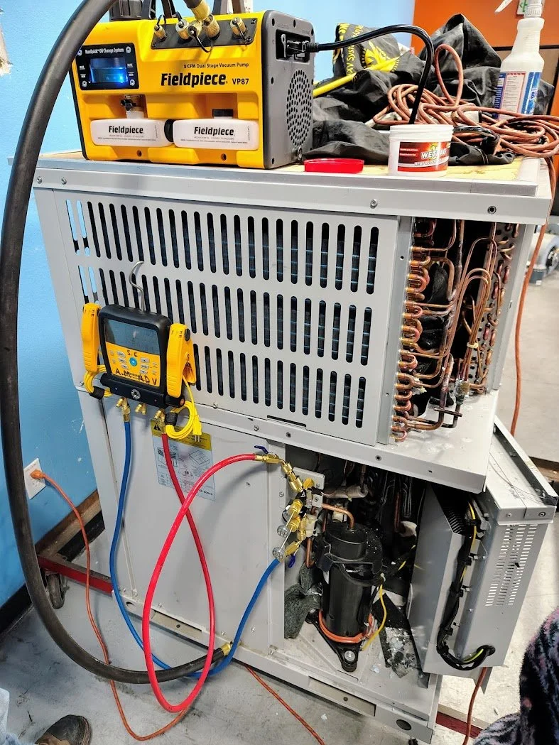 A refrigeration or HVAC system with copper tubing, compressor, and control components, with tools and a yellow vacuum pump on top, indicating maintenance or repair work.