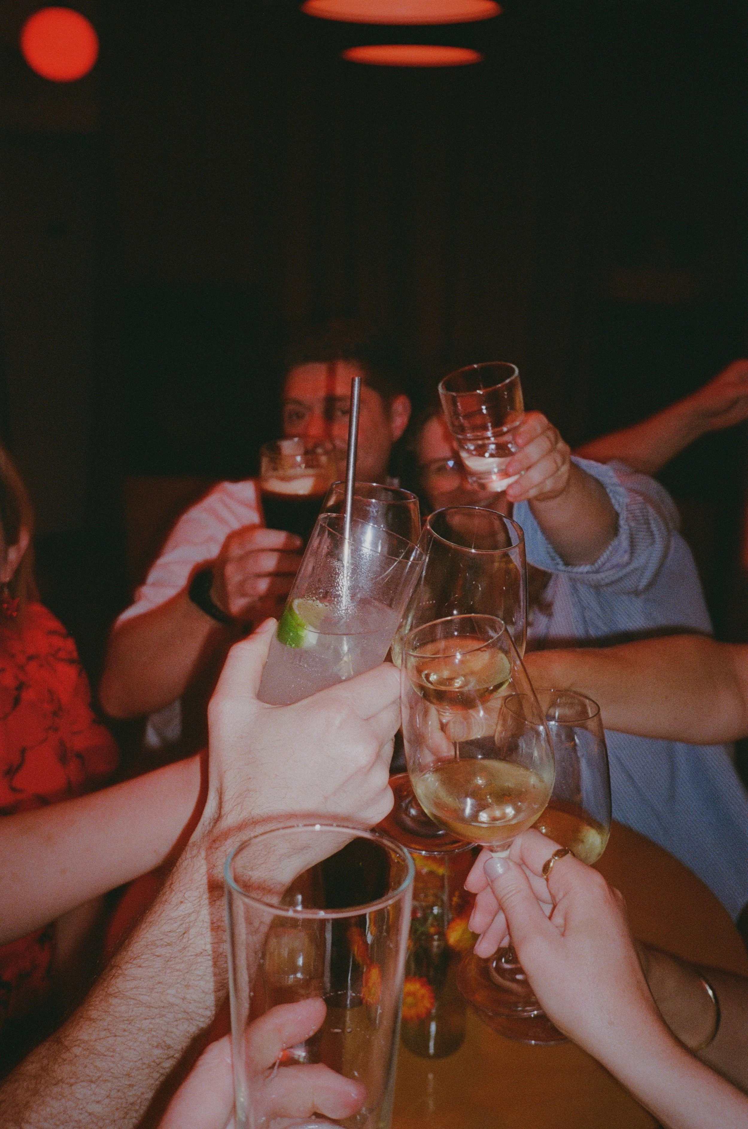People clinking glasses of drinks during a celebration or party in a dimly lit setting.