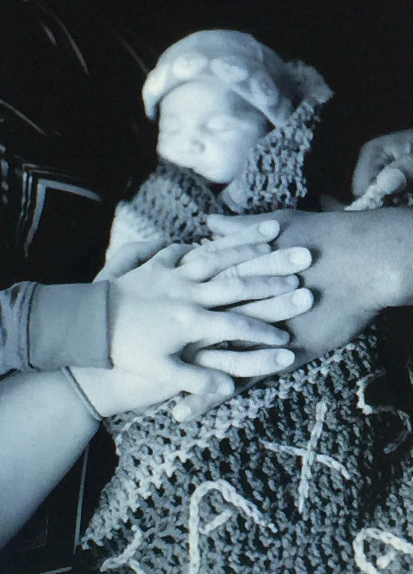 A newborn baby is being fed while multiple hands support the baby's head and body in a close-up scene.