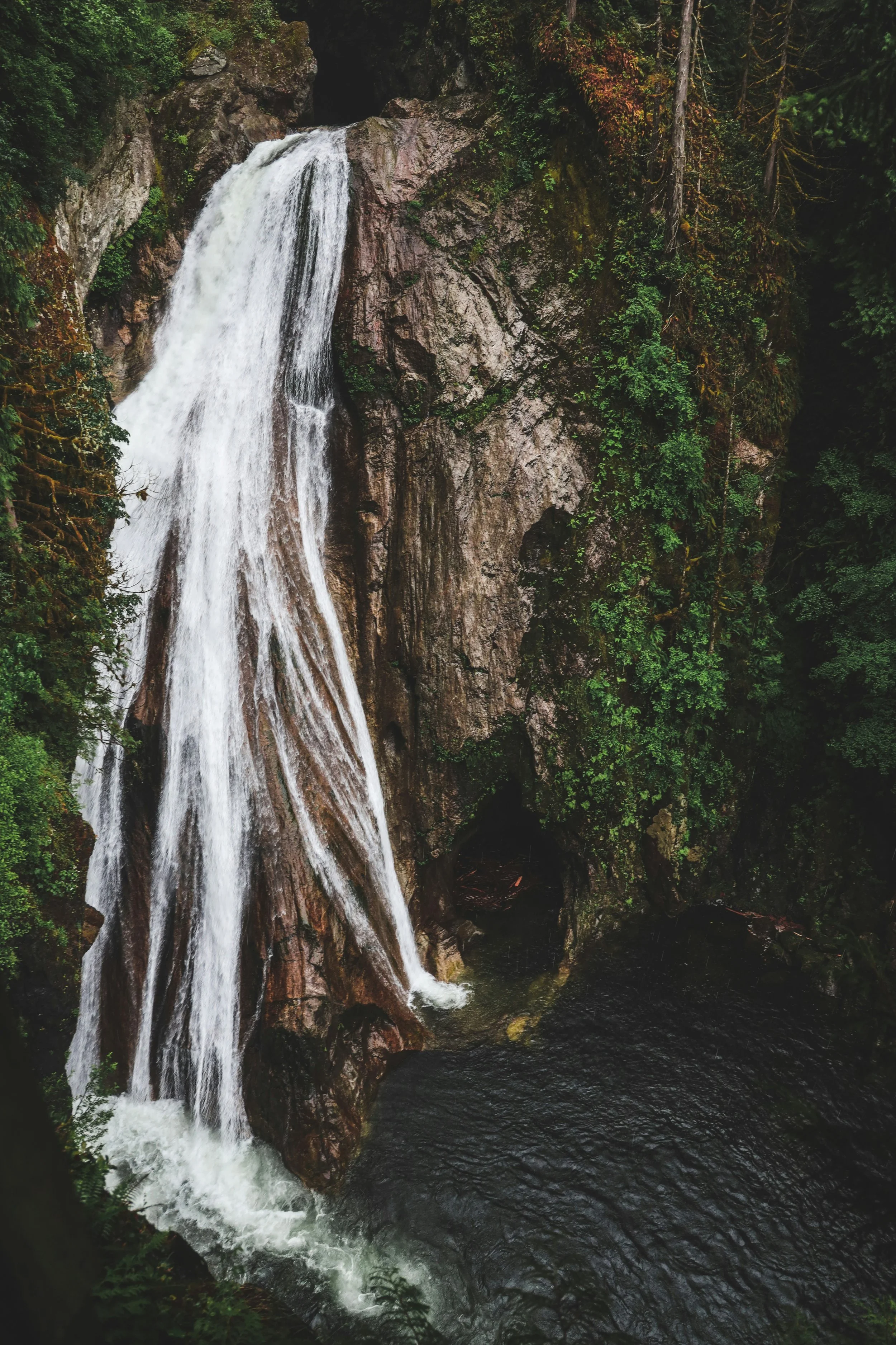 A scenic waterfall flowing down a rocky cliff surrounded by lush green forest.