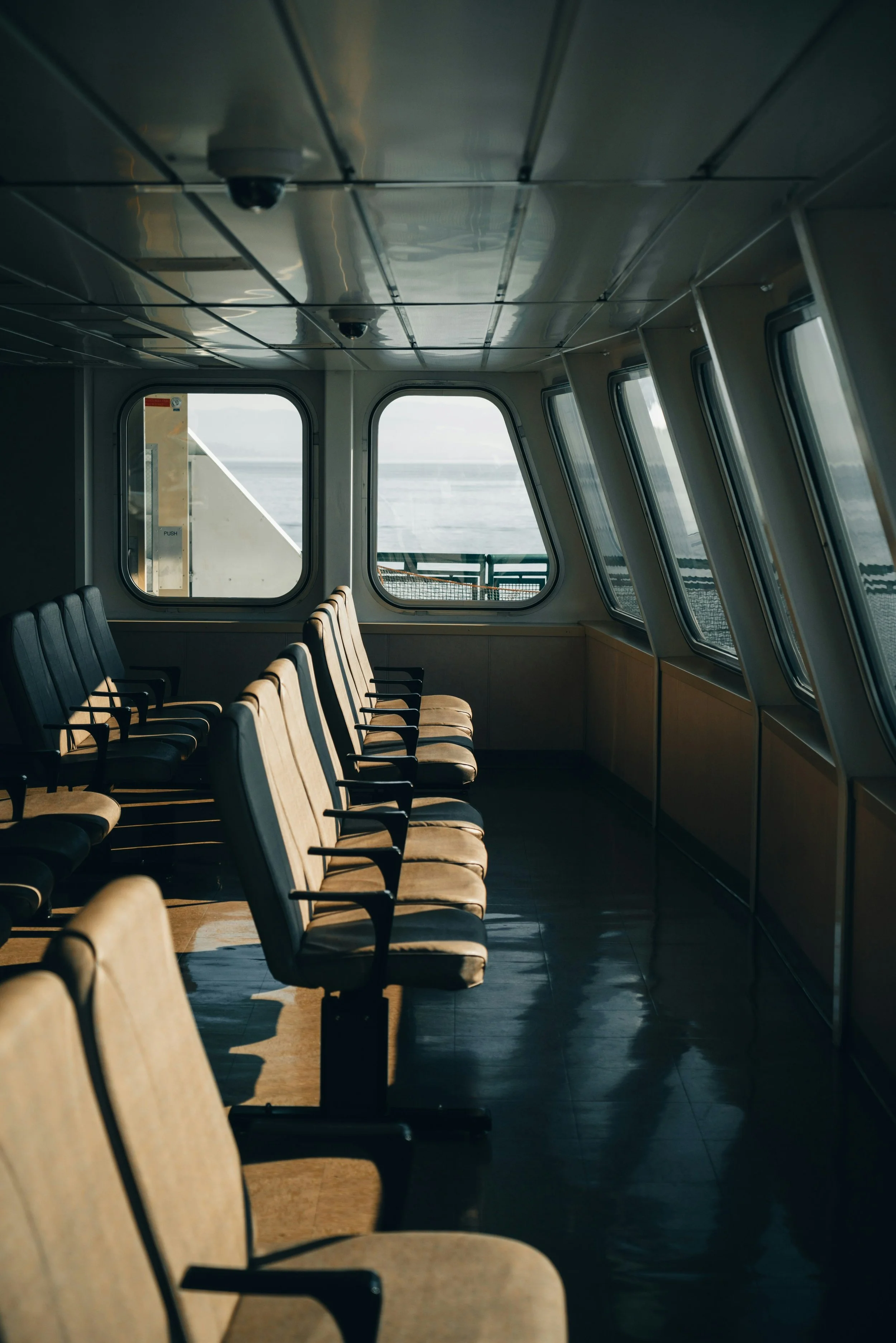 Empty chairs inside a ferry or ship cabin, with windows showing water outside.