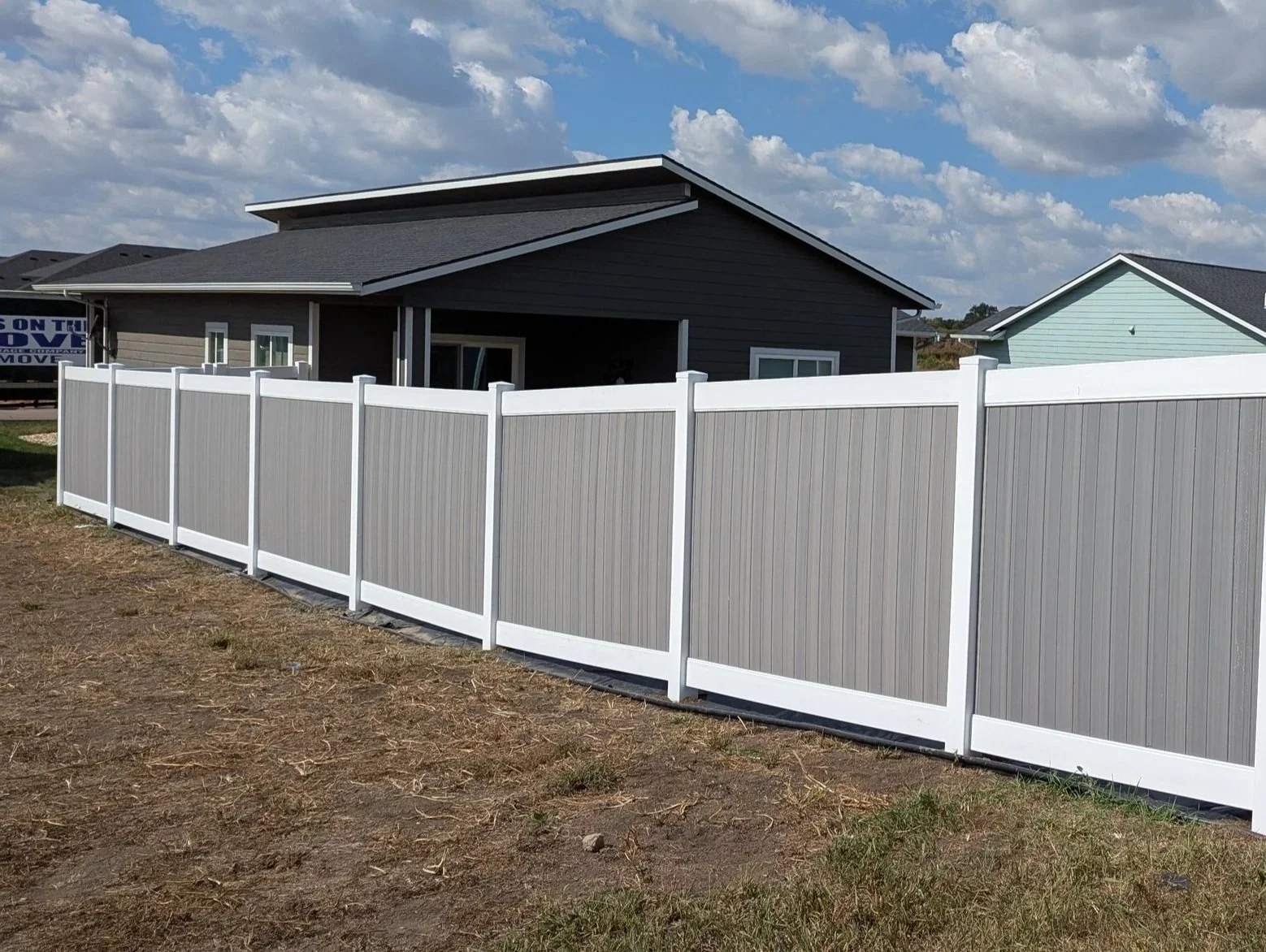 Newly installed gray vinyl privacy fence around a backyard with a modern house and partly cloudy sky.