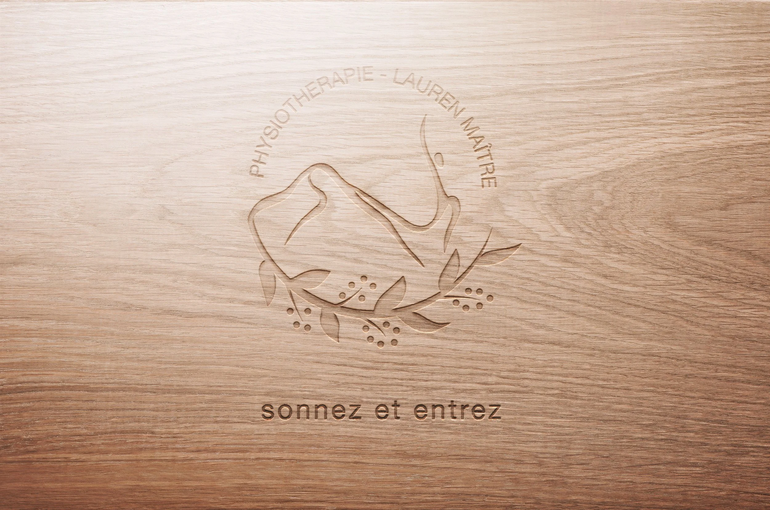 Une plaque en bois gravée avec un design de main tenant une branche et des petits fruits, comportant le texte "PHYSIOTHERAPIE - LAUREN MÀITRE" en arc autour, et "sonnez et entrez" en dessous.
