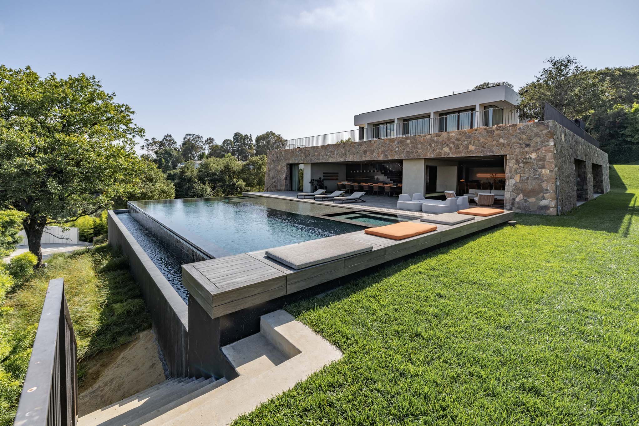 Modern house with an infinity pool on a grassy yard, surrounded by trees and a clear sky