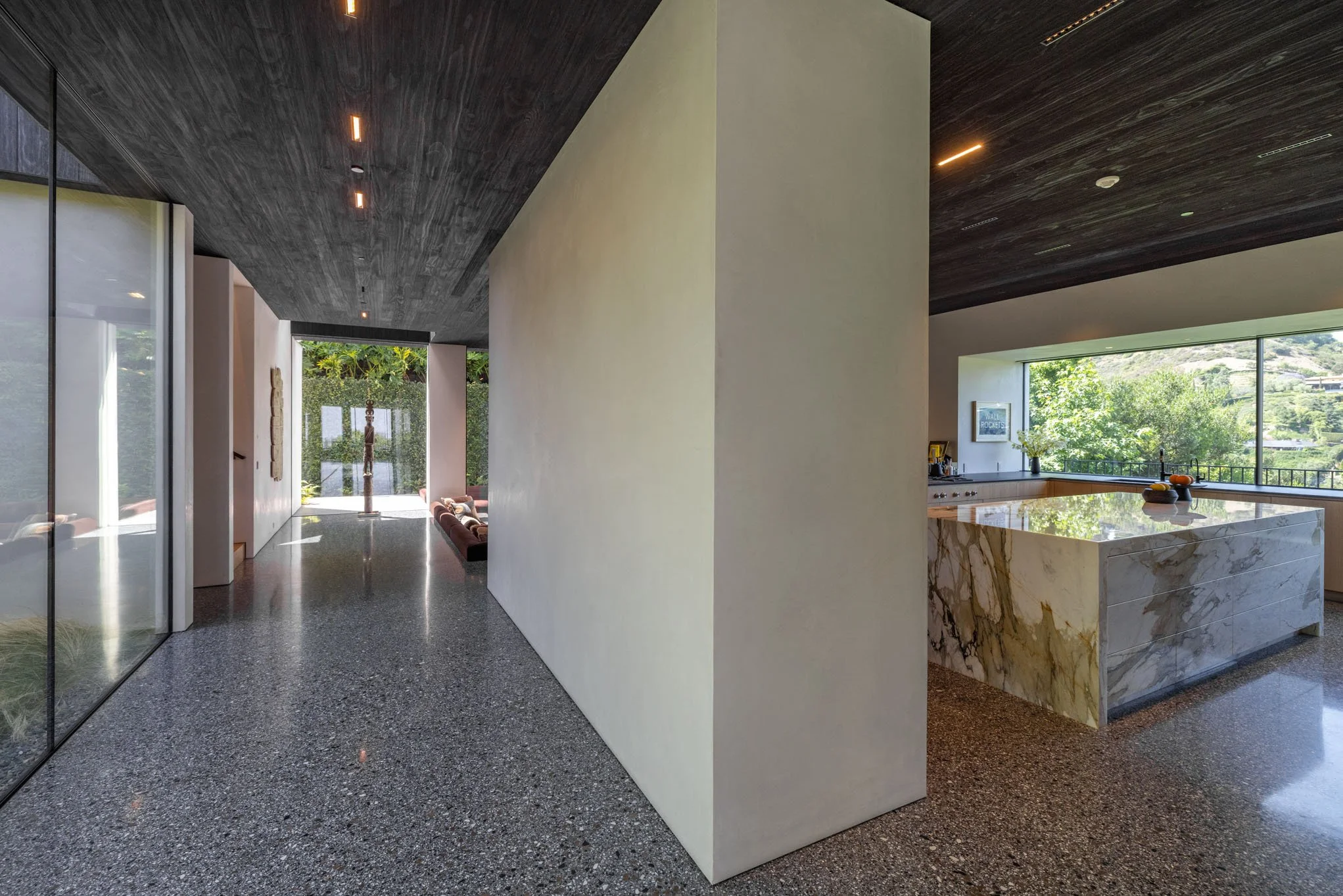 Modern interior of a house with a hallway, large glass windows, and a kitchen island with a marble top.