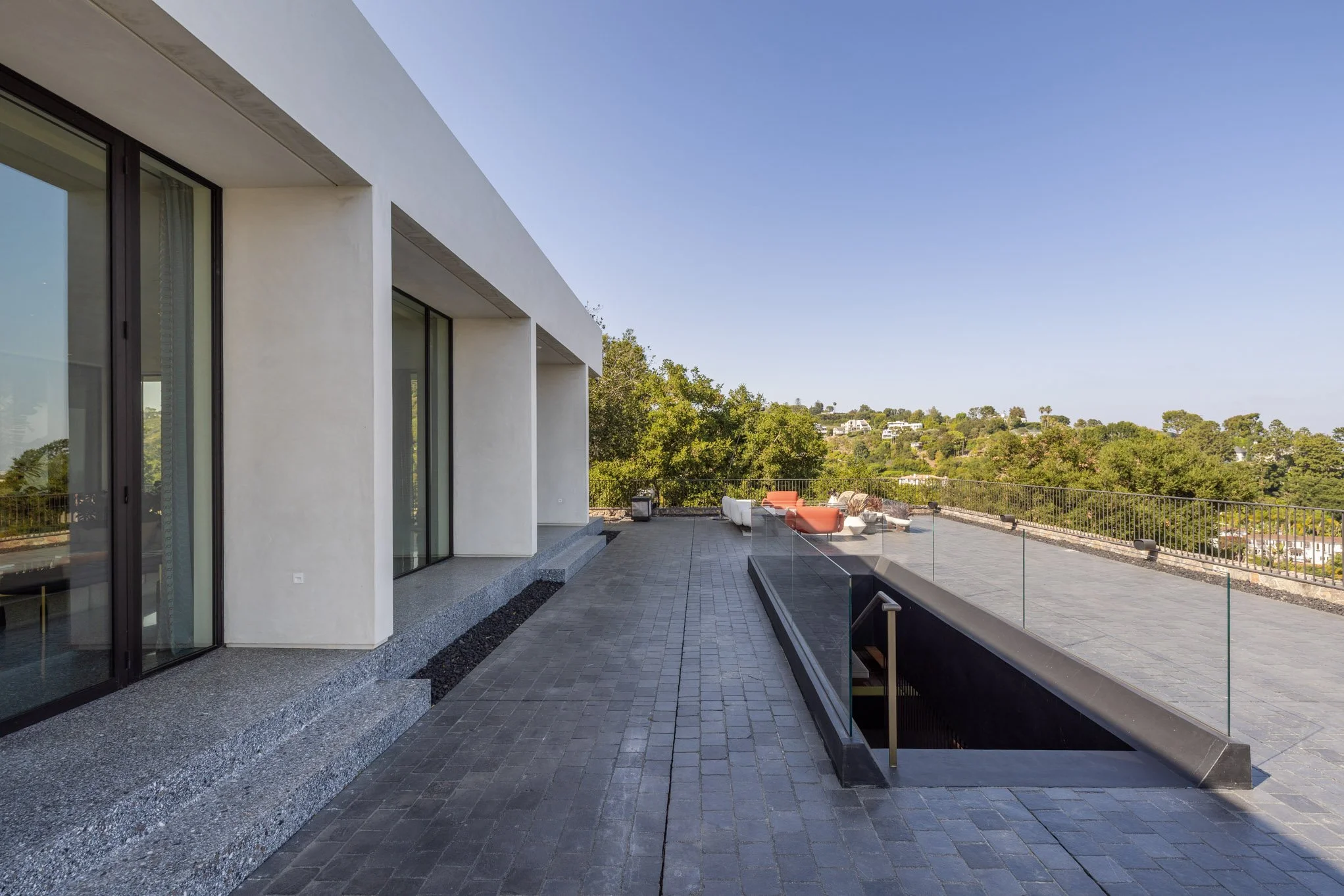 Modern house rooftop terrace with outdoor seating, glass railing, and scenic view of trees and hills.