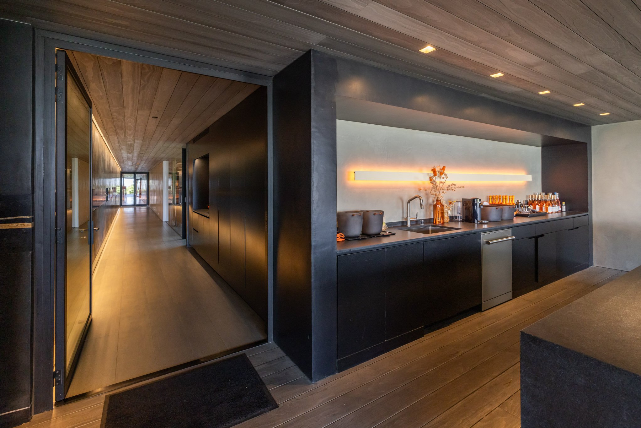 Modern hotel or office kitchenette with dark cabinetry, a sink, and ambient lighting.