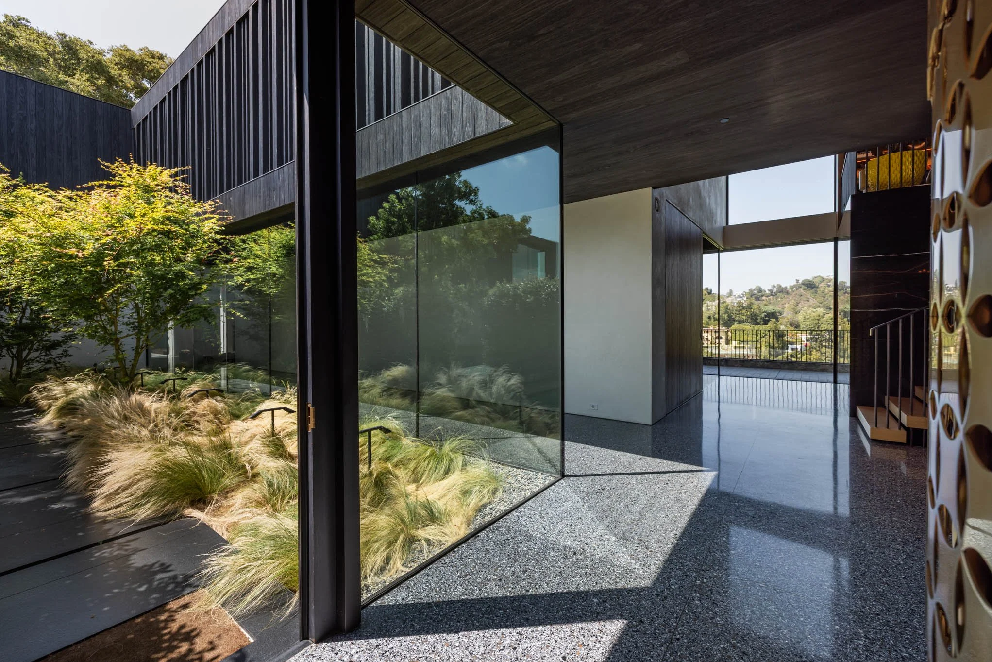 Modern interior with large glass windows overlooking greenery, terrazzo flooring, and designer wall accents.