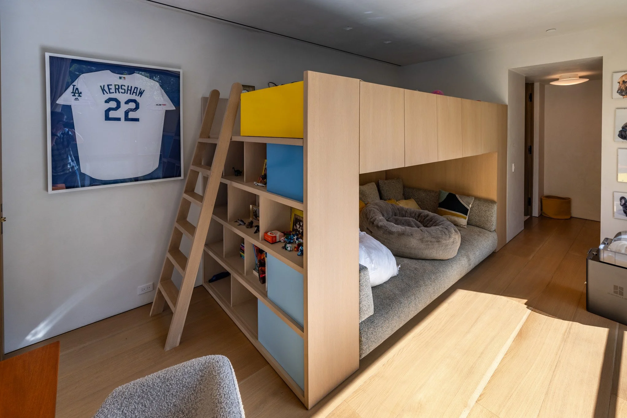 Living room with a custom wooden sofa bed and a bookshelf, decorated with a framed baseball jersey of Kershaw, number 22, and a ladder leaning against the wall.