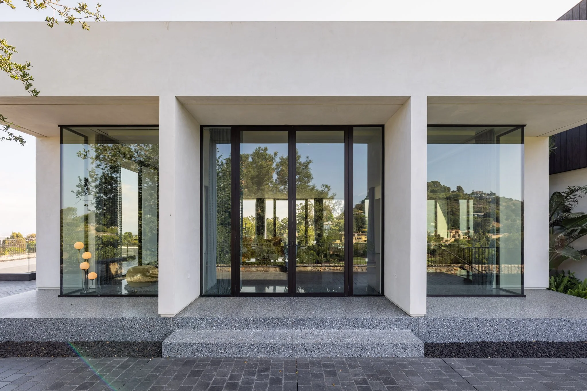Front view of a modern house with large glass doors and windows, white exterior walls, and small steps leading up to a platform.