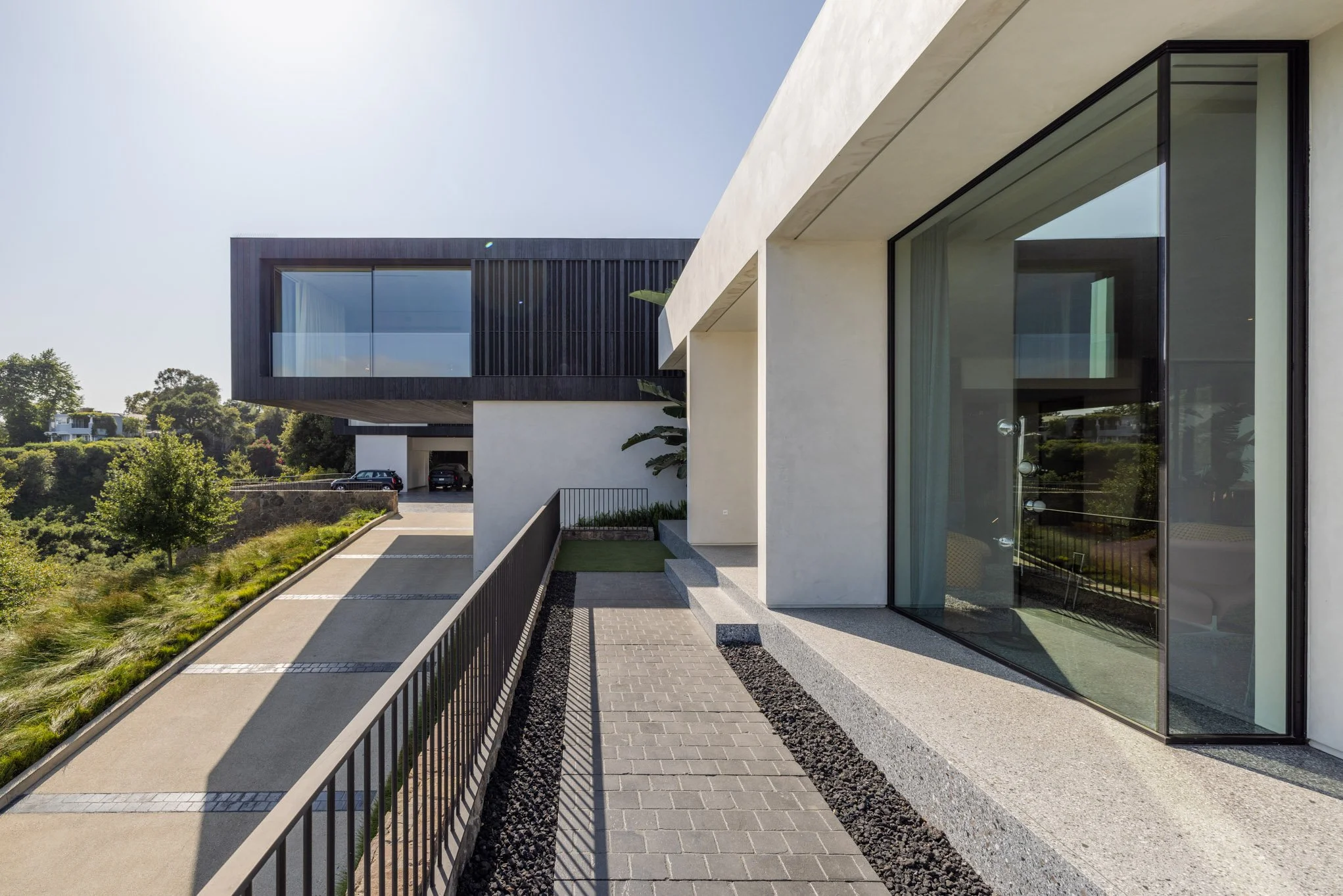 Modern residential building with large glass windows, concrete and black wood exterior, and a sloped driveway leading to a garage