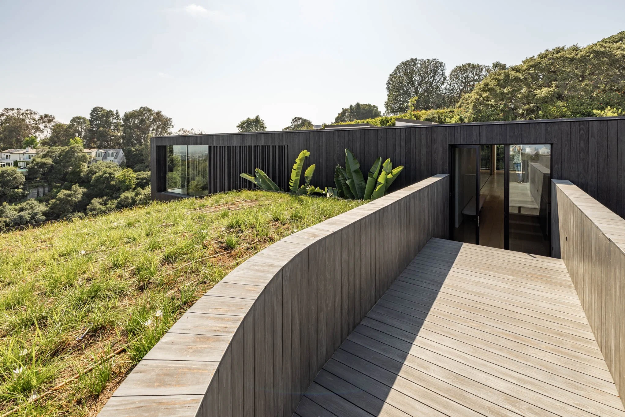 Modern house with black exterior walls, glass doors, and surrounding greenery on a hillside.