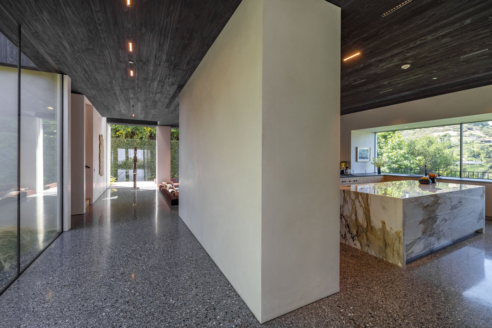 Modern interior of a house with a hallway, large glass windows, and a kitchen island with a marble top.