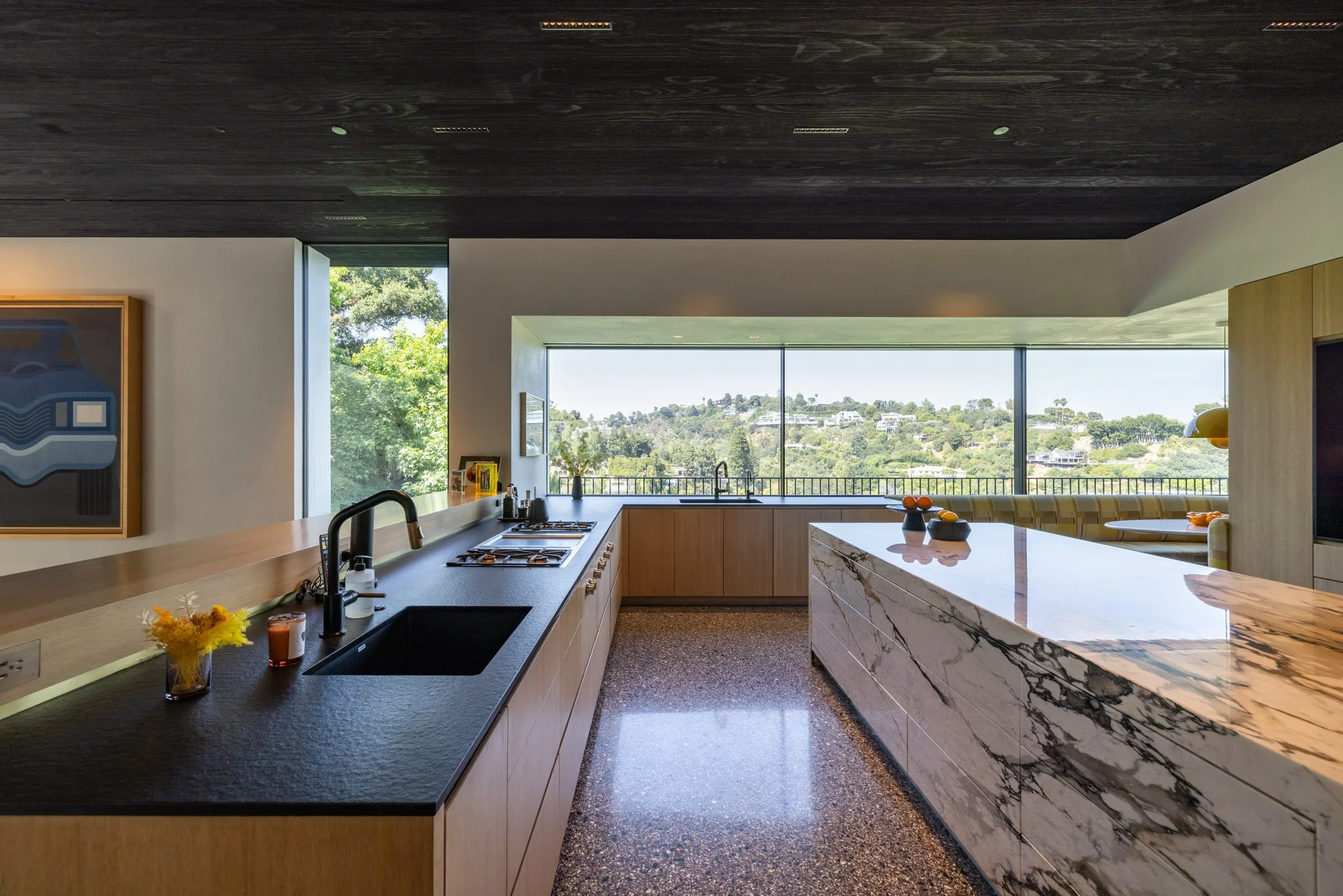 Modern kitchen with black countertops, wooden cabinets, marble island, large window view of green landscape, and black sink