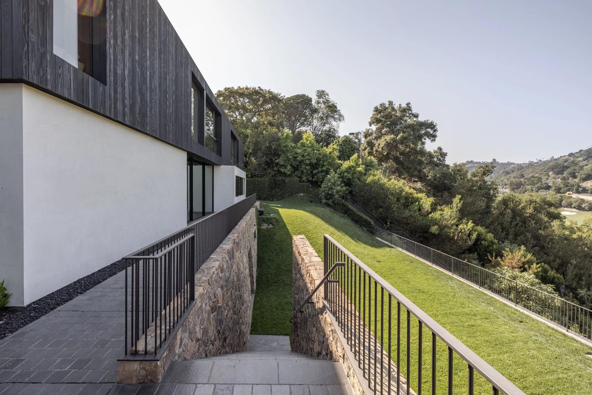 Modern multi-story house with black and white exterior walls, surrounded by a lush green landscape and trees in the distance.