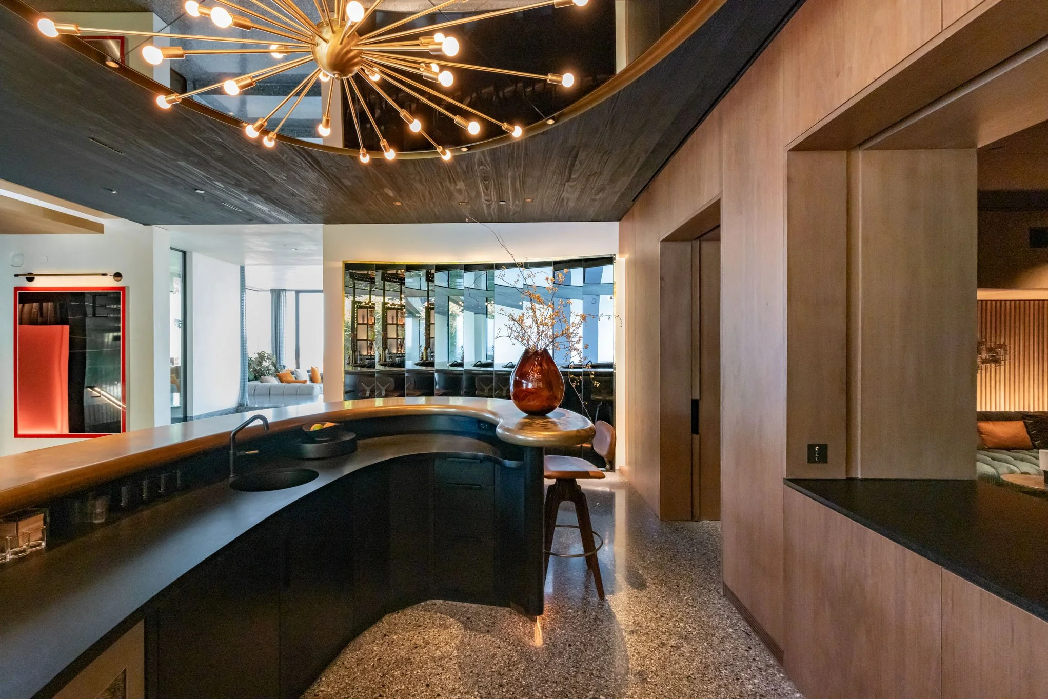 Modern kitchen with wooden accents, black countertop, decorative vase with branches, round barstool, and a starburst chandelier