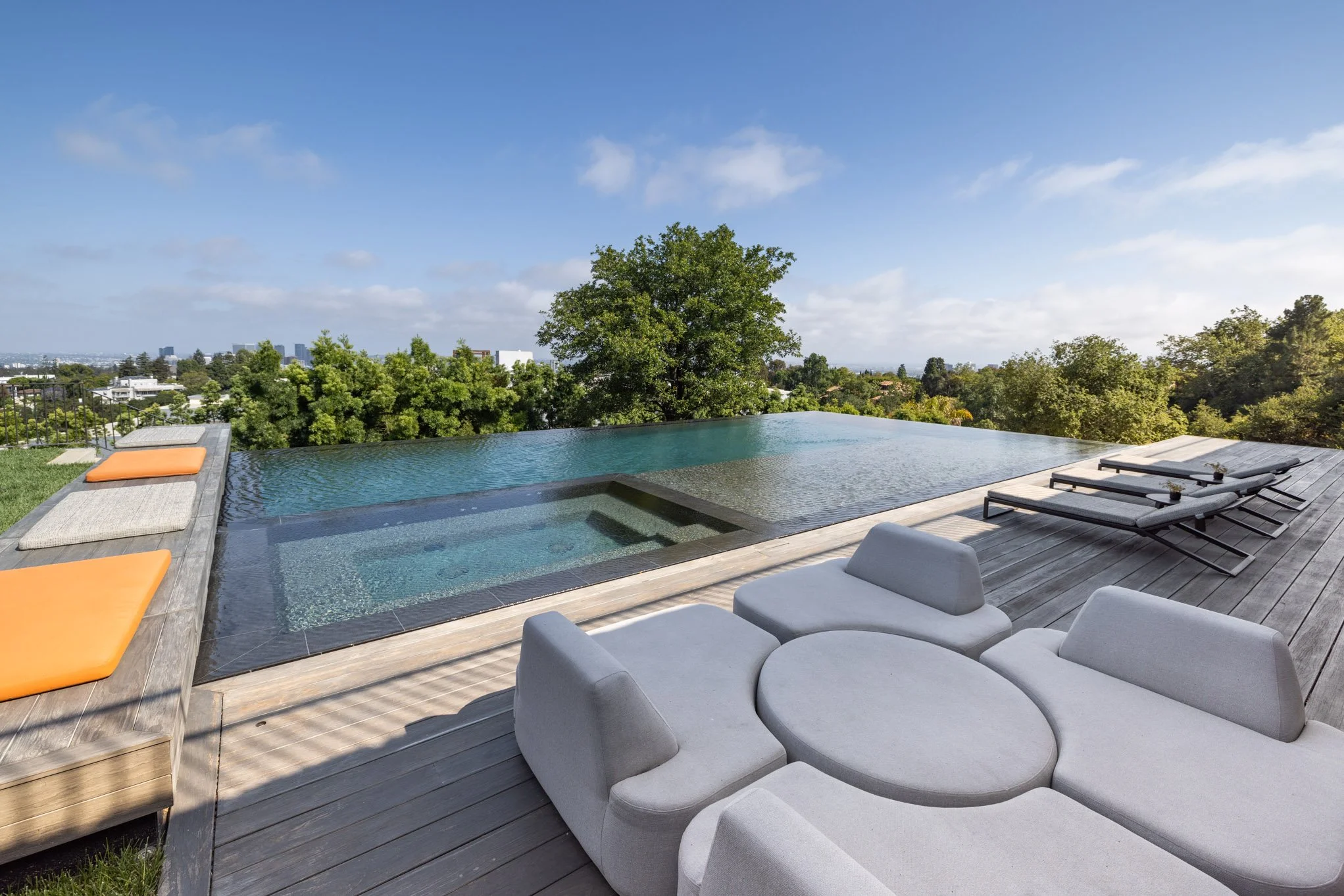 Luxury rooftop infinity pool with sun loungers, cushioned seating, and a scenic city view.