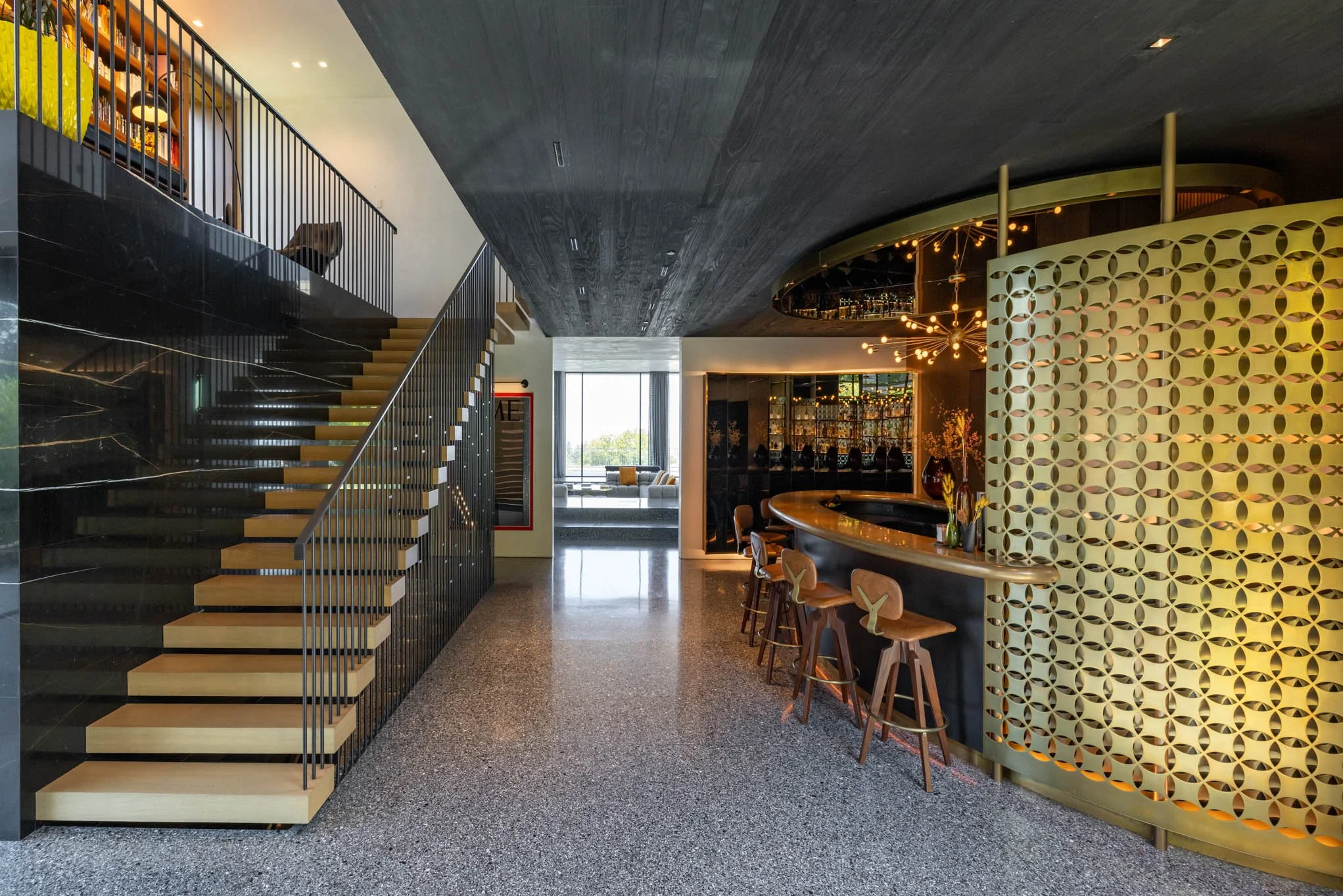 Modern hotel lobby with a staircase, bar area, and seating cabinet near large window.