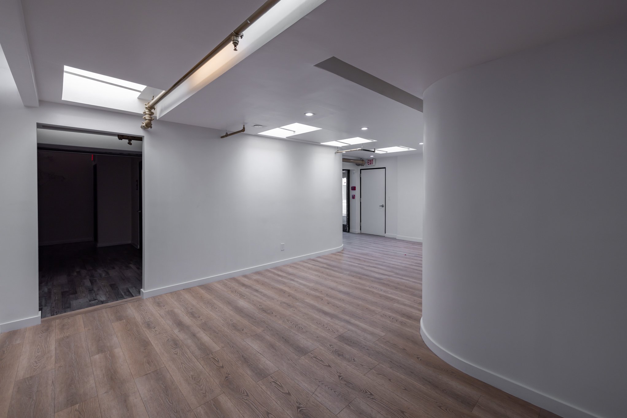 Empty modern interior space with white walls, wooden flooring, and ceiling skylights.