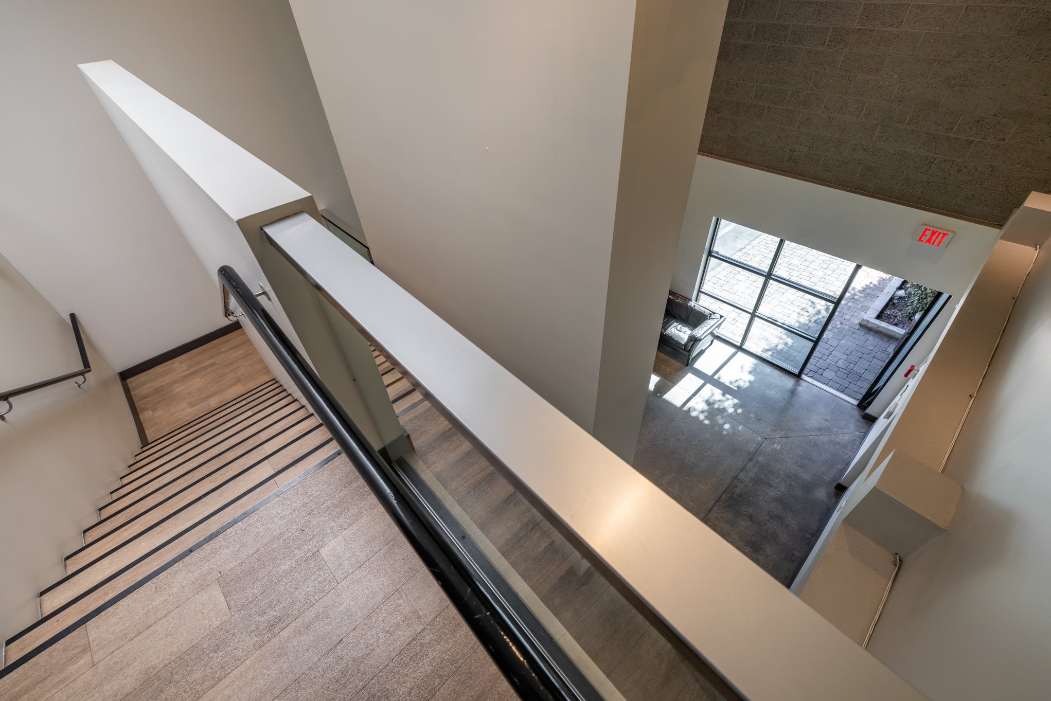 View from the top of a staircase looking down toward an exit door with glass panels and a bench outside.